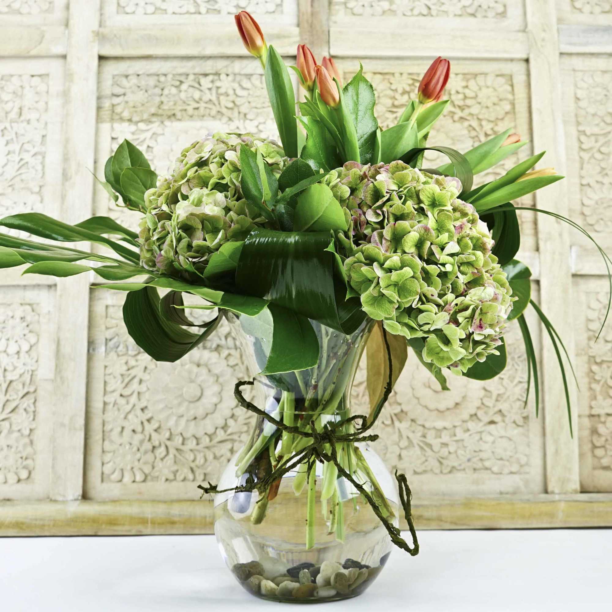 Green hydrangeas and orange tulips in a clear glass vase