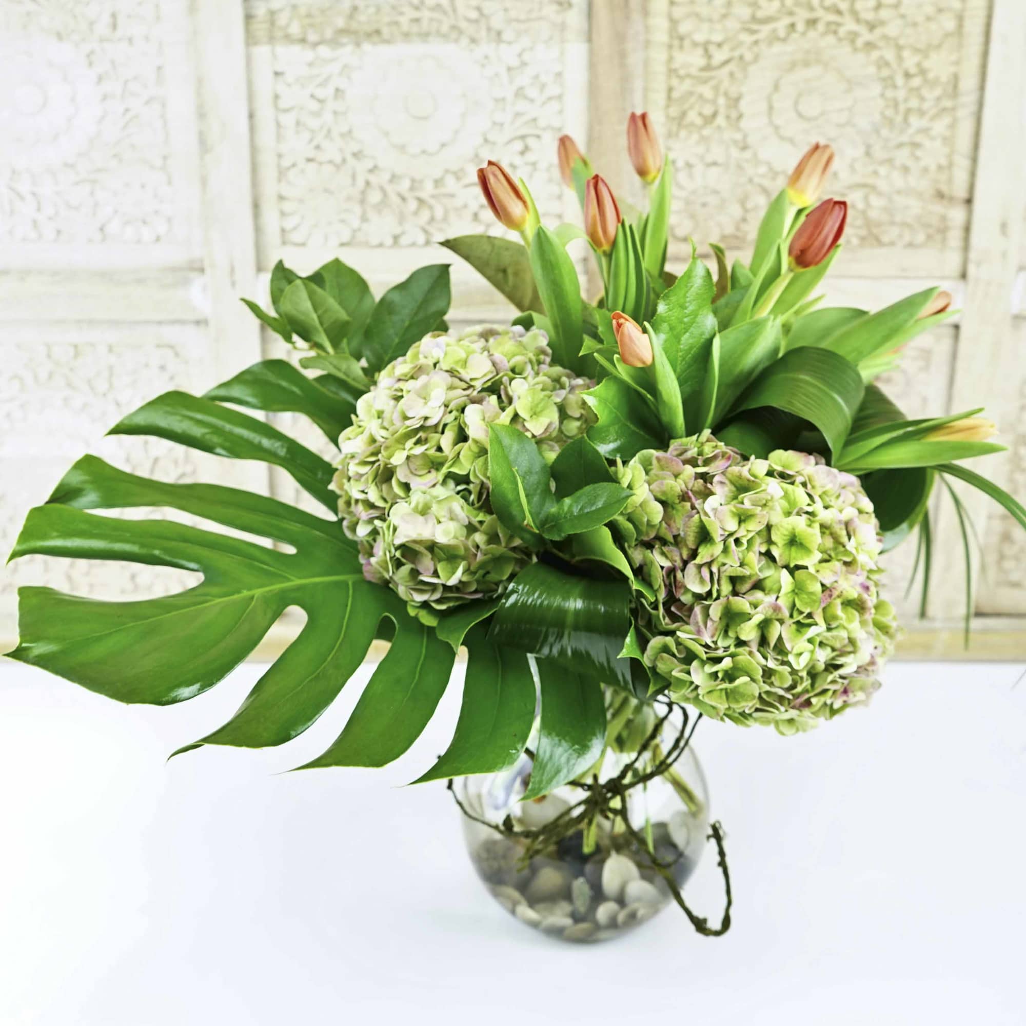Hydrangeas and tulip buds in a glass vase with large tropical leaves