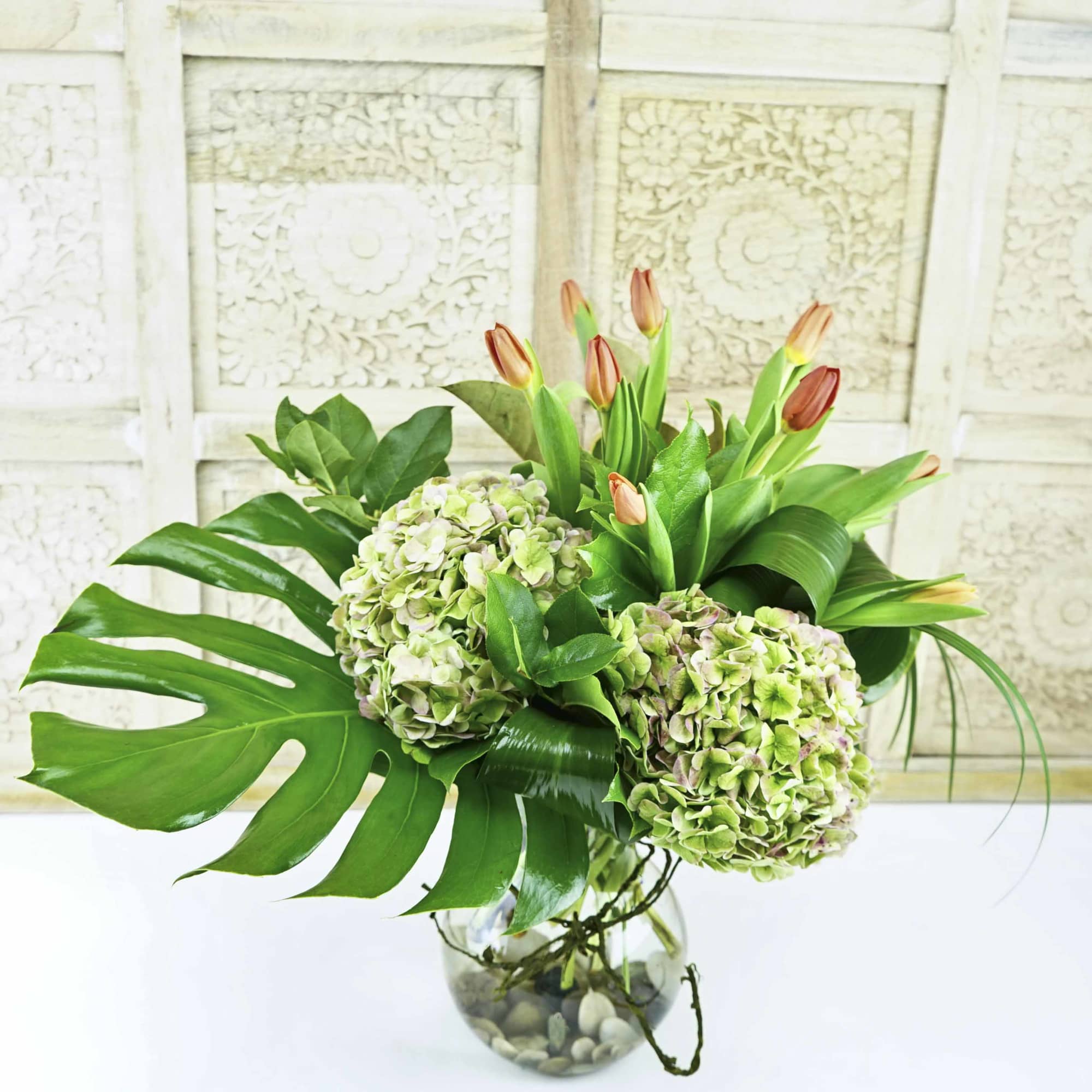 Green hydrangeas and tulip buds arranged in a glass vase