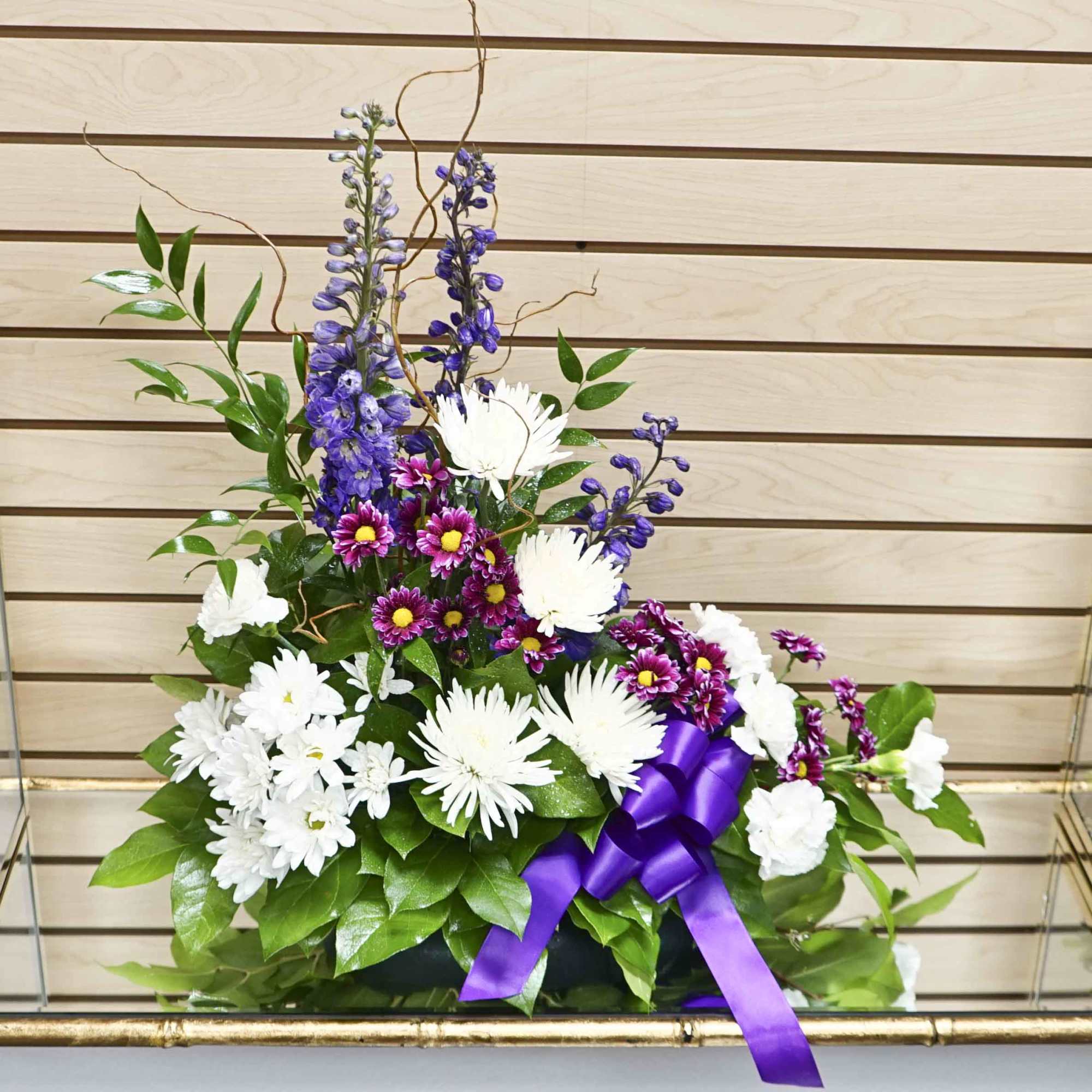 Purple, white, and blue floral arrangement with a purple ribbon