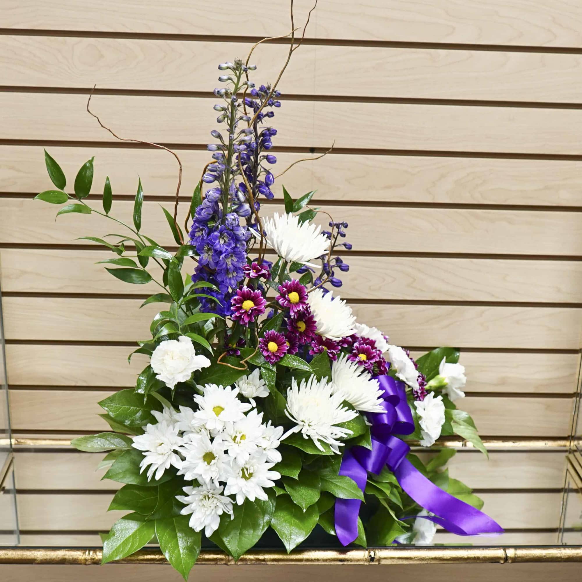 Tall floral arrangement with white daisies, purple flowers, and a purple ribbon