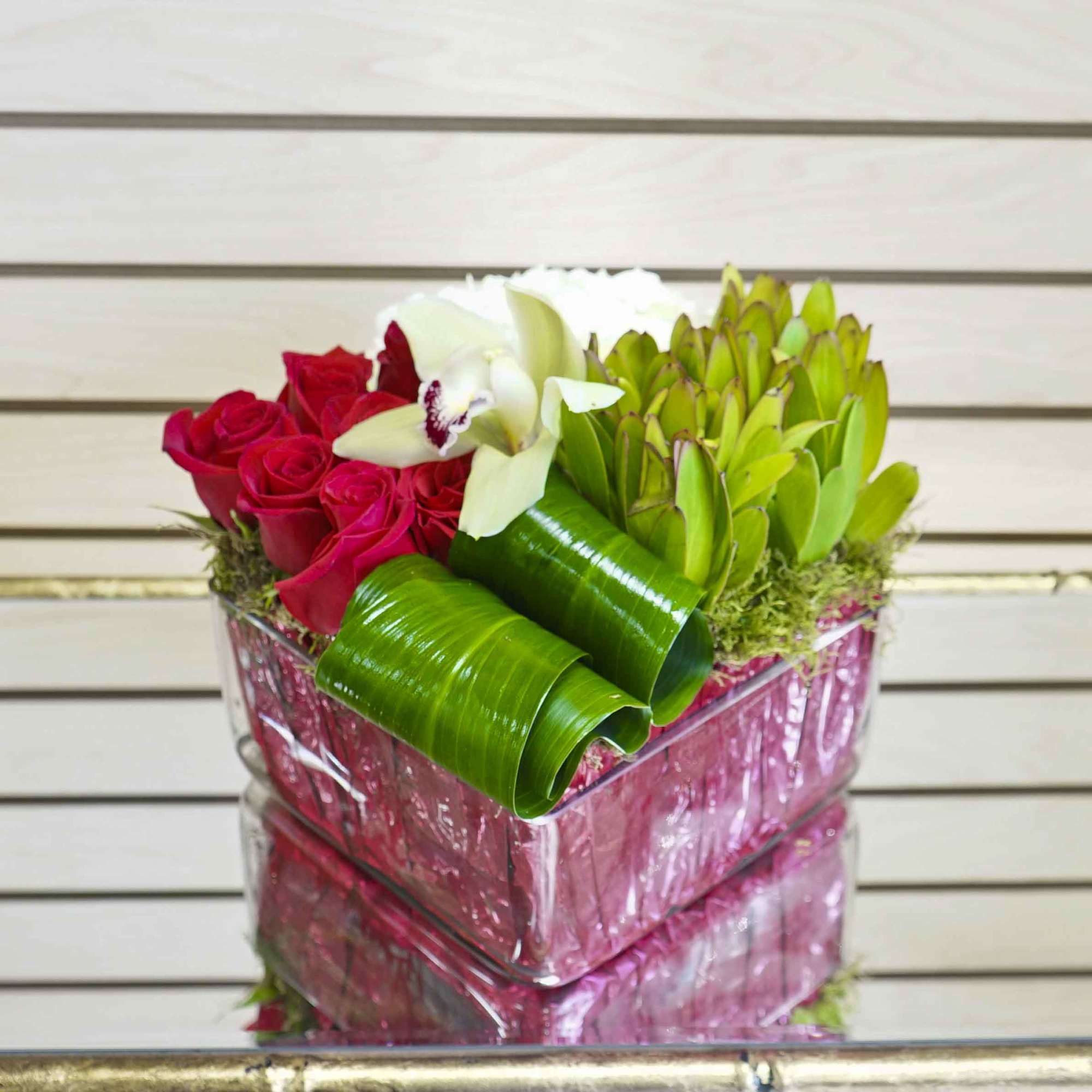 Pink box arrangement with red roses, white orchid, and green tropical leaves