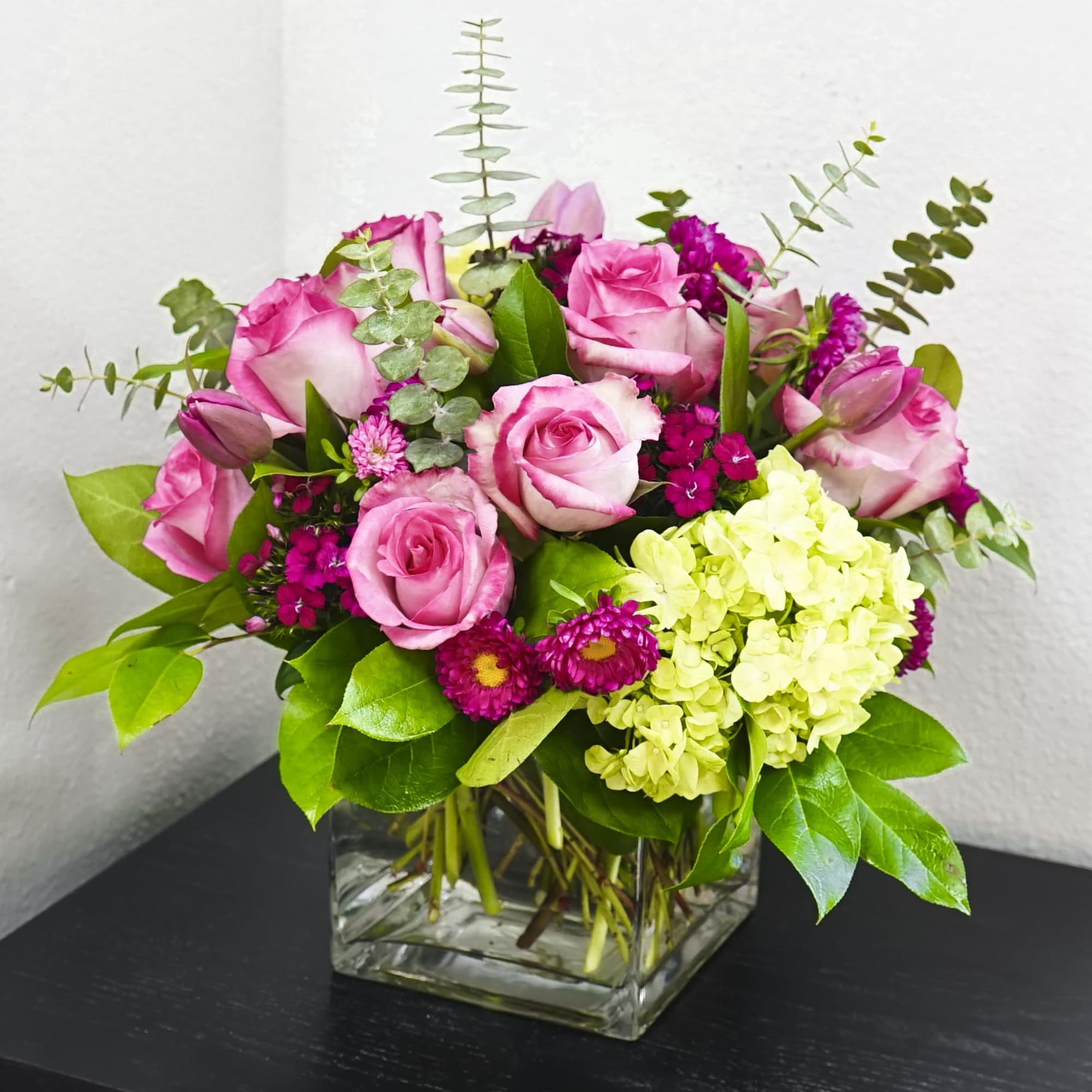 Pink roses and magenta flowers in a square glass vase