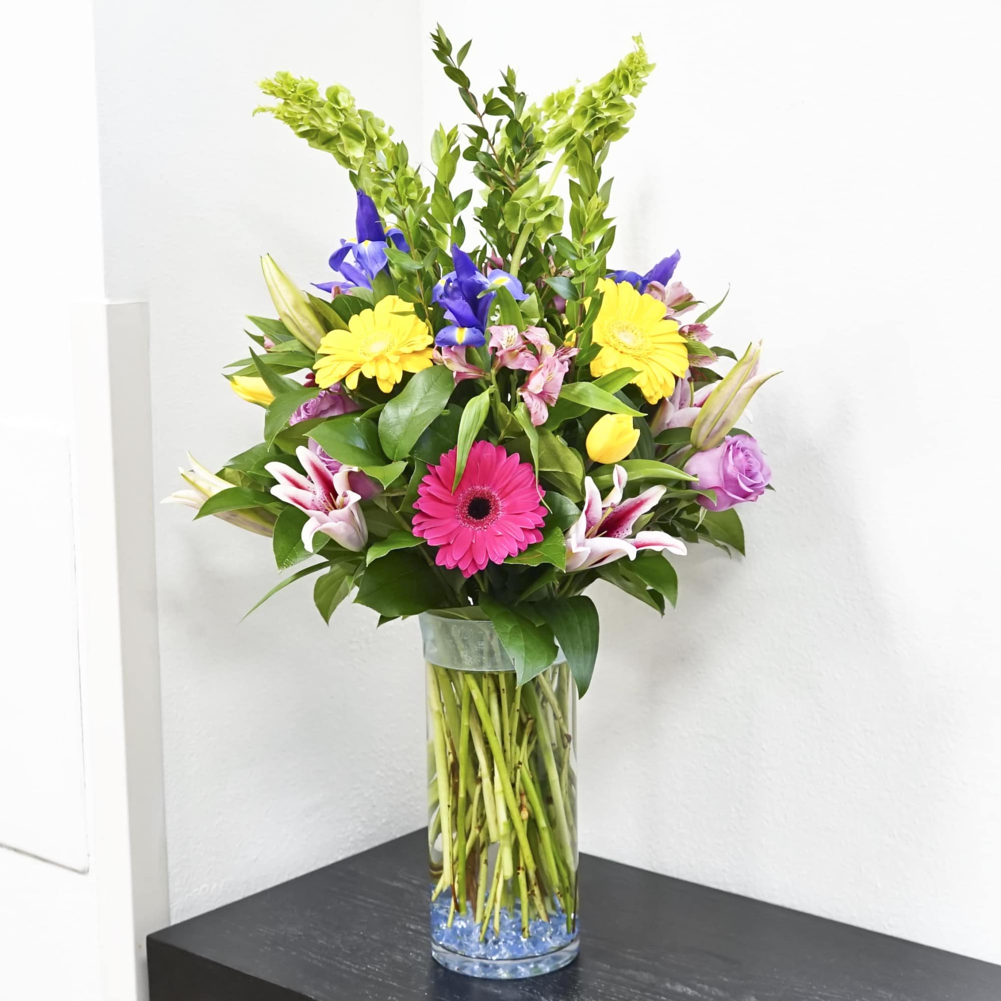 Mixed bouquet in a clear glass vase with bright yellow, pink, purple, and white flowers