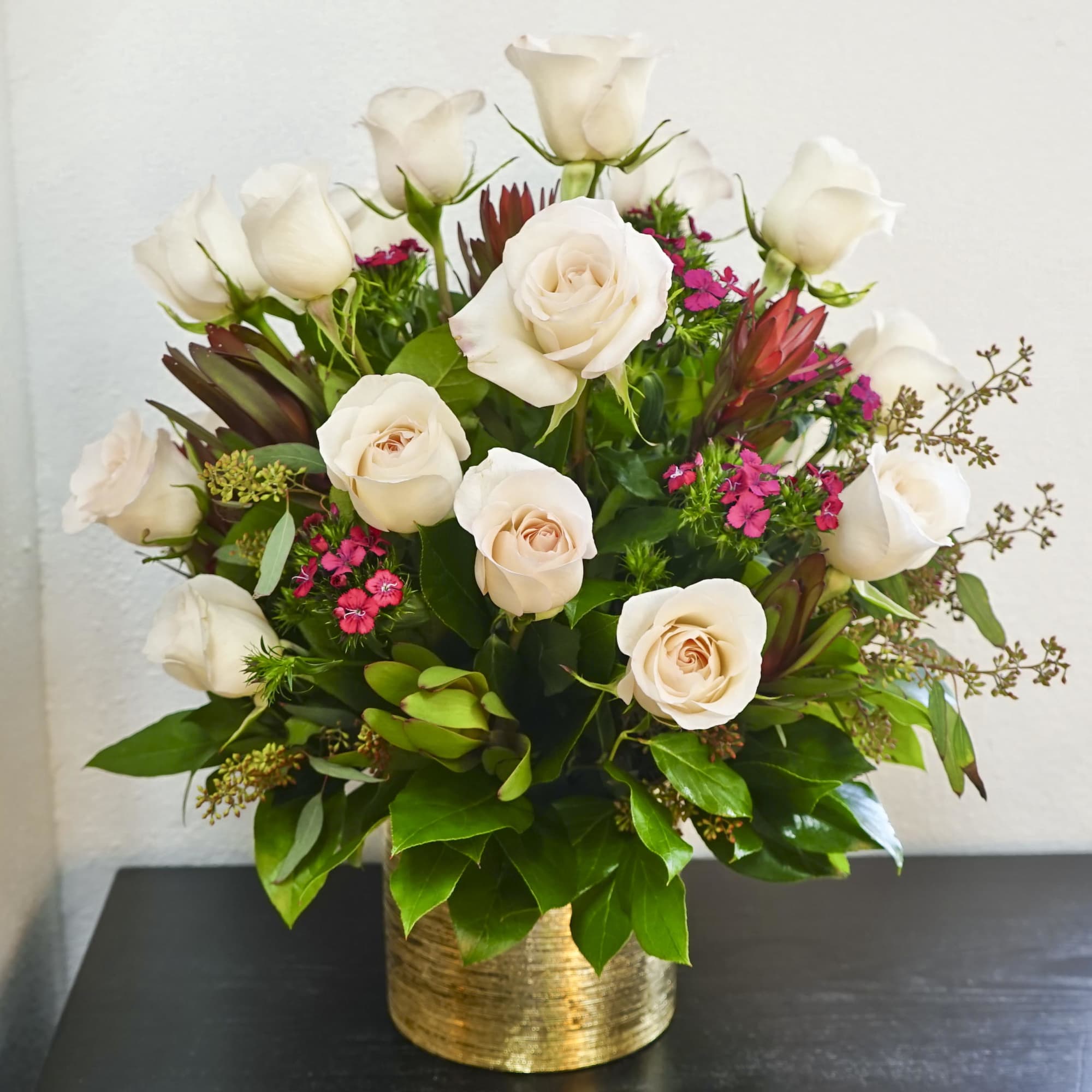 Cream roses arranged in a gold vase with pink filler flowers