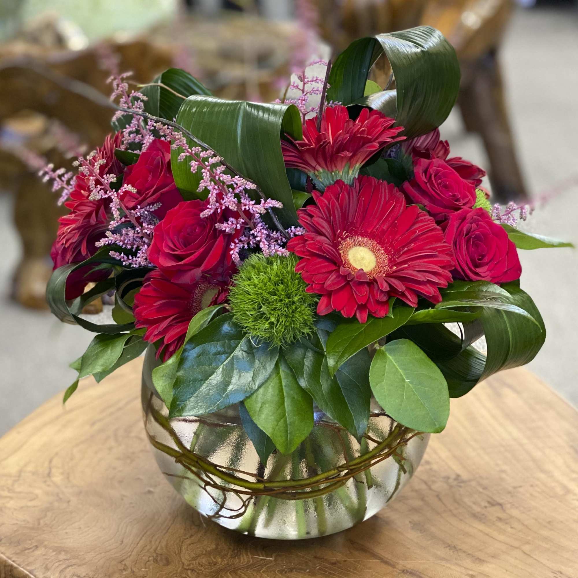 Red roses and gerbera daisies in a glass vase with green foliage