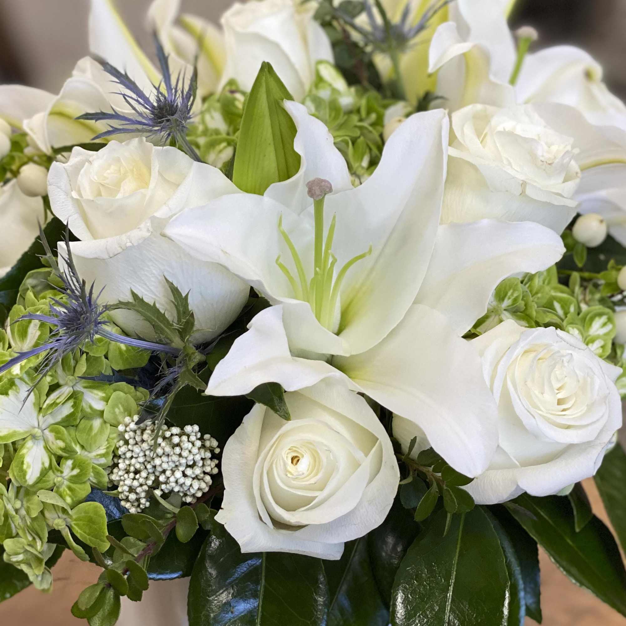 White lilies and roses arranged with green hydrangeas and blue thistle