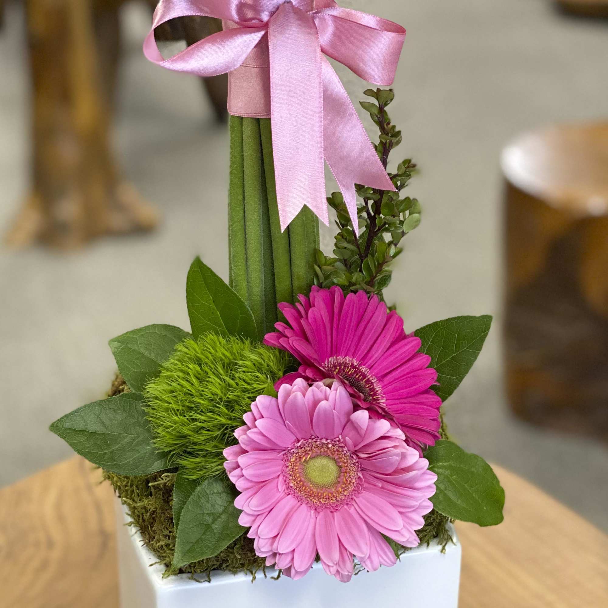 Pink gerbera daisies with a ribbon on a small white container