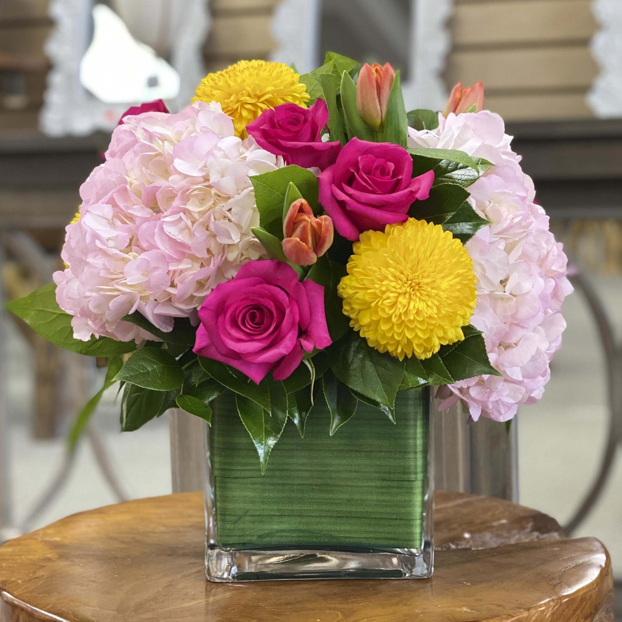 Pink roses and hydrangeas with yellow mums in a square glass vase