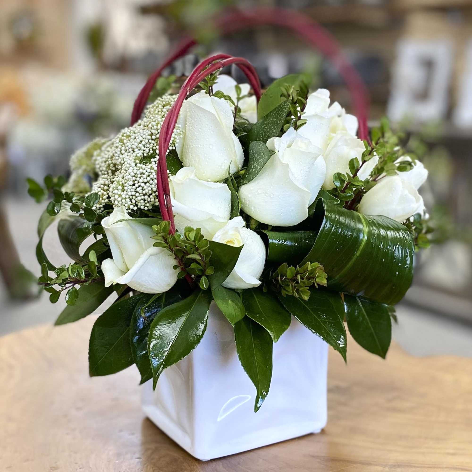 White rose arrangement in a white square vase with red handles