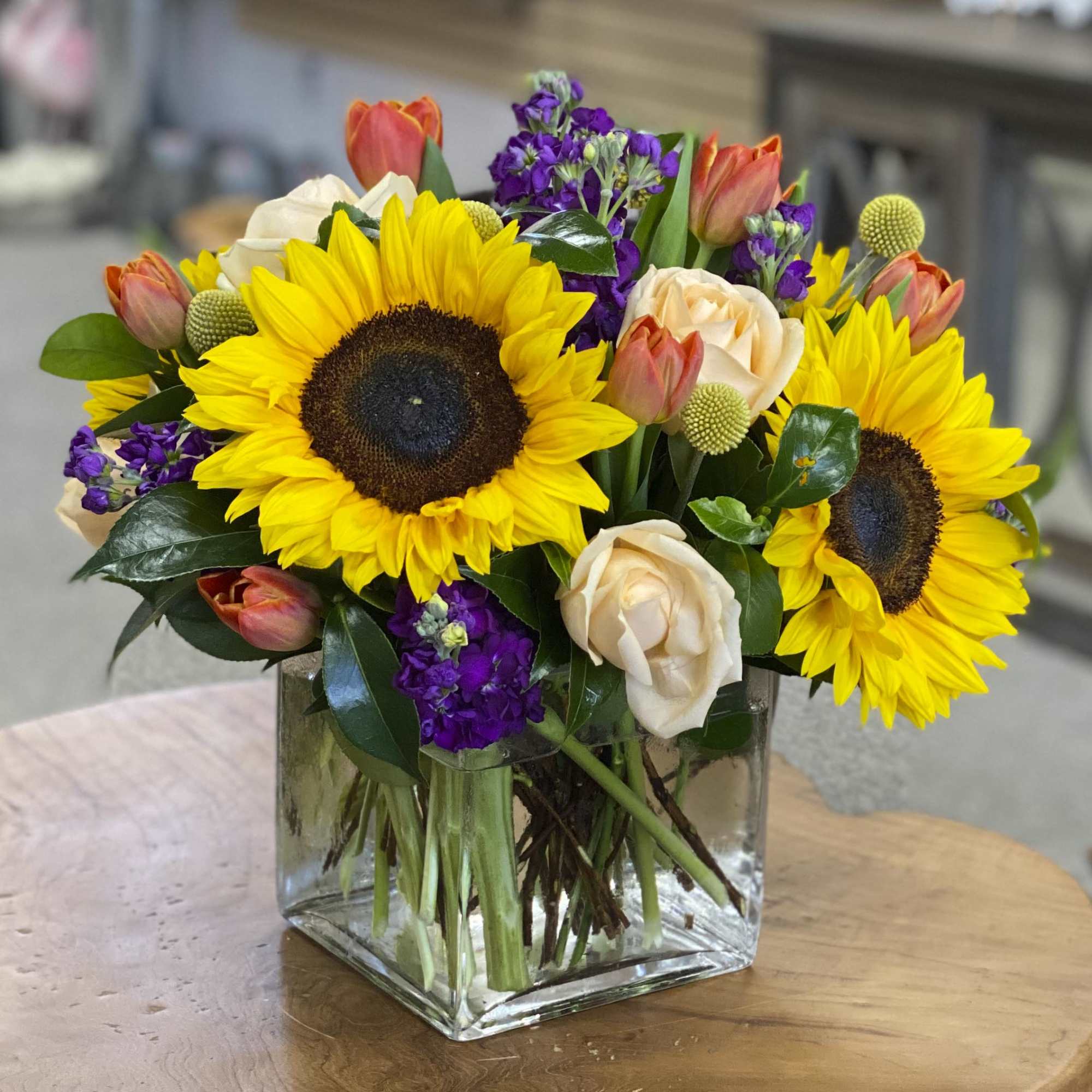 Bouquet of sunflowers, roses, tulips, and purple flowers in a glass vase