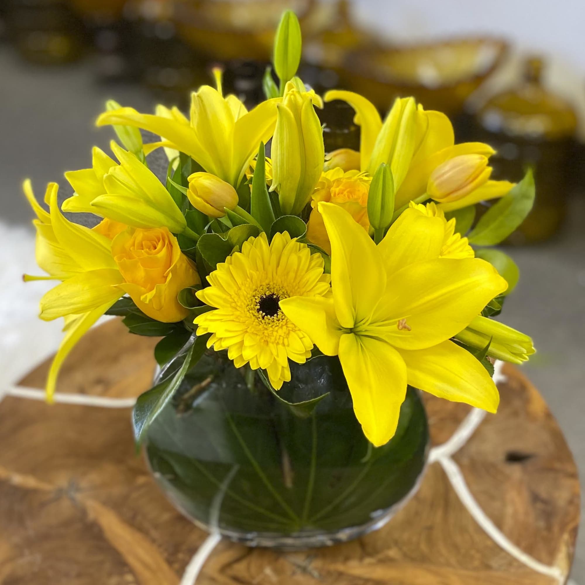 Yellow lilies and gerbera daisies in a round glass vase