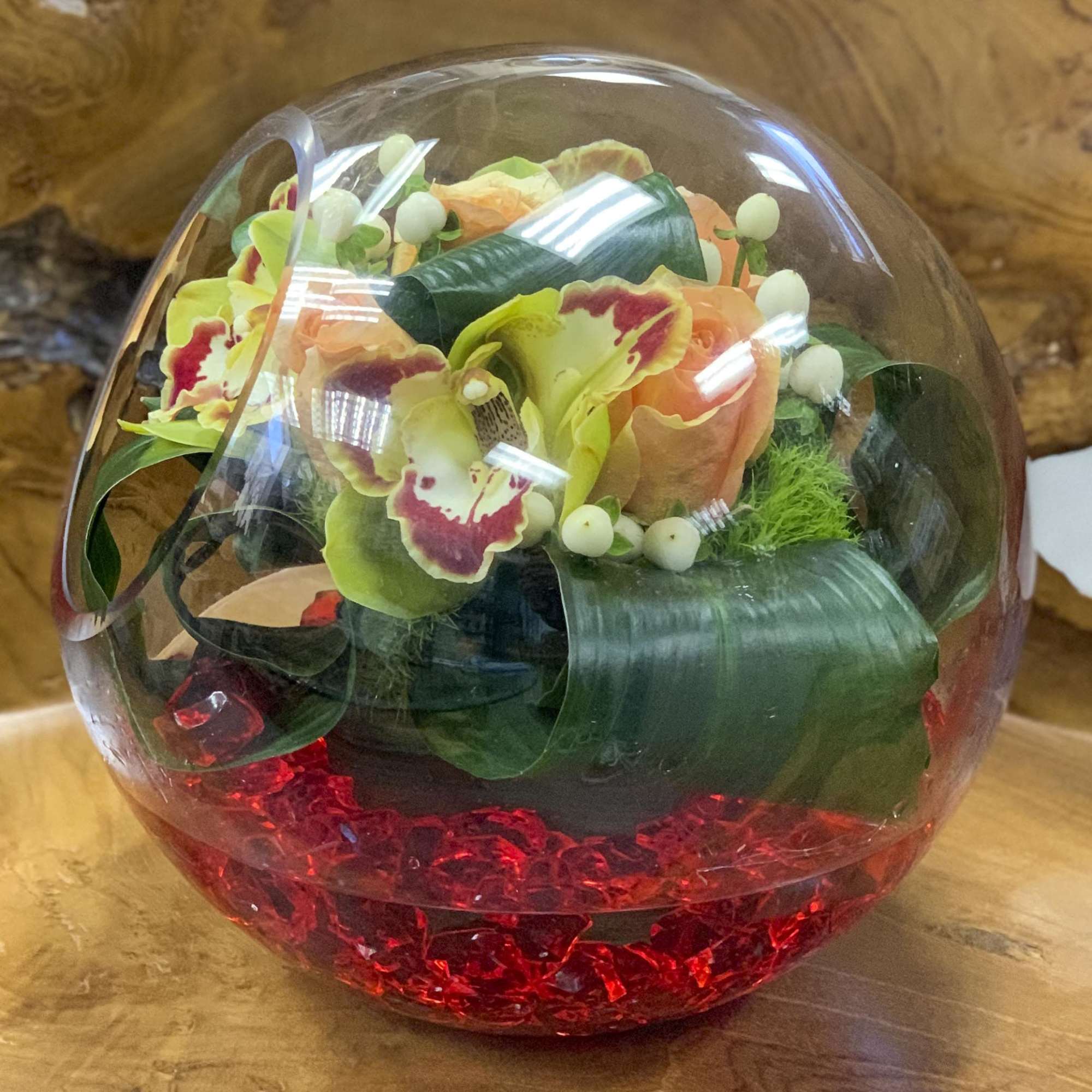 Floral arrangement in a clear glass orb with red stones at the base