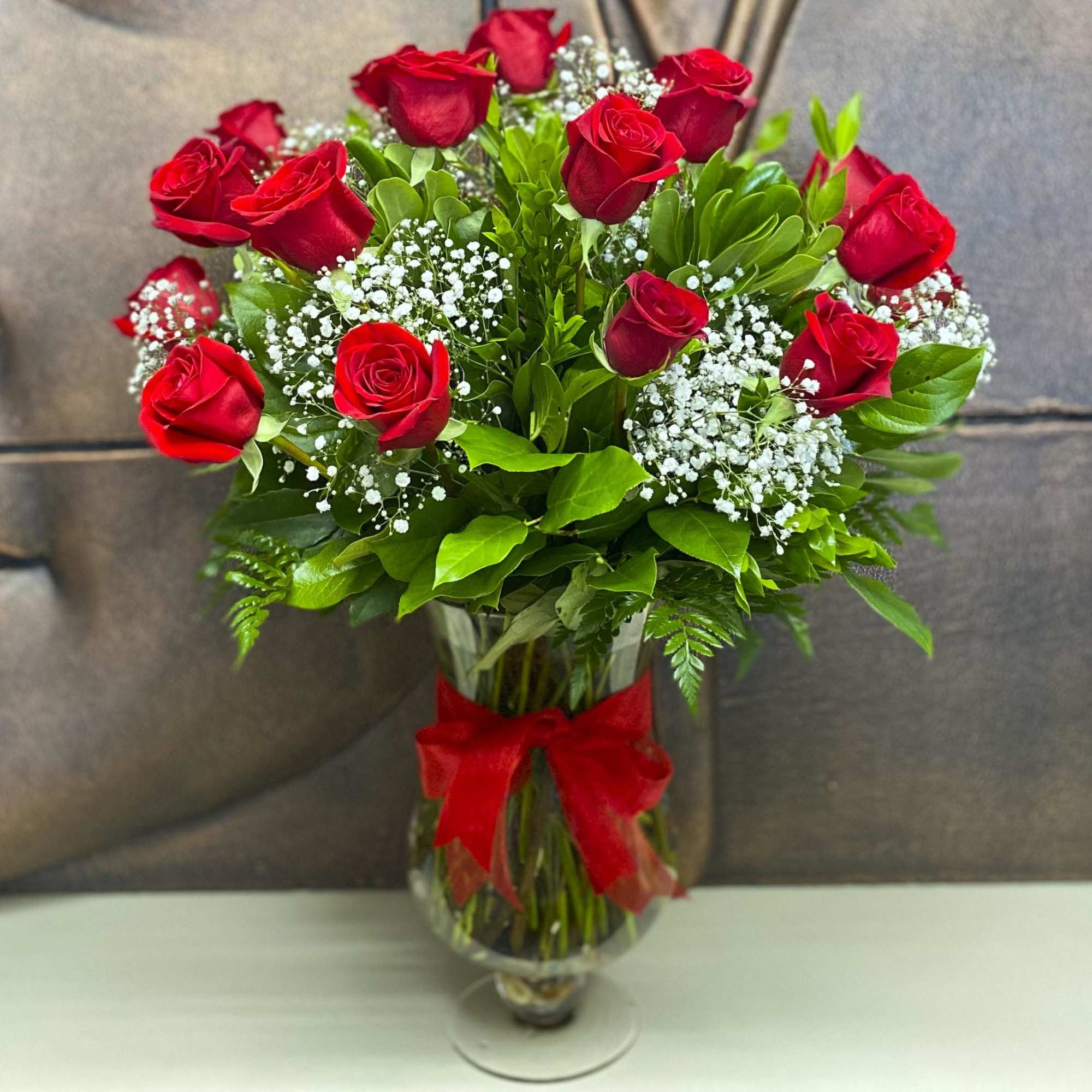 Red roses arranged in a clear glass vase with a red ribbon