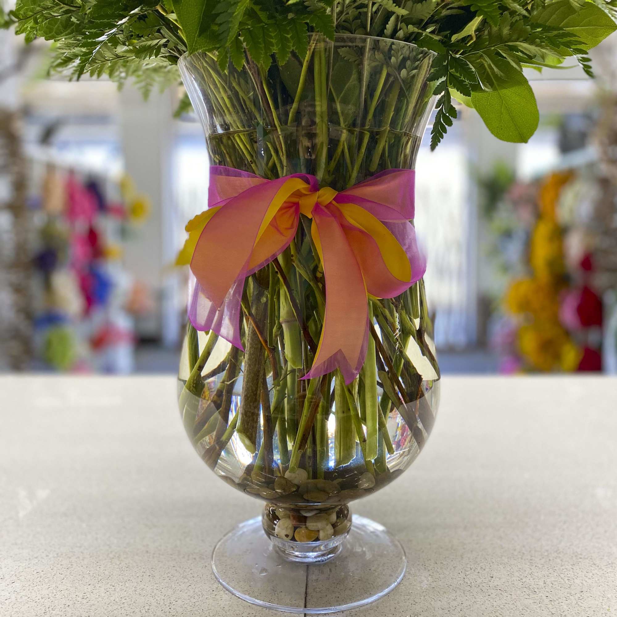 Green floral stems in a clear glass vase tied with a pink and orange ribbon.
