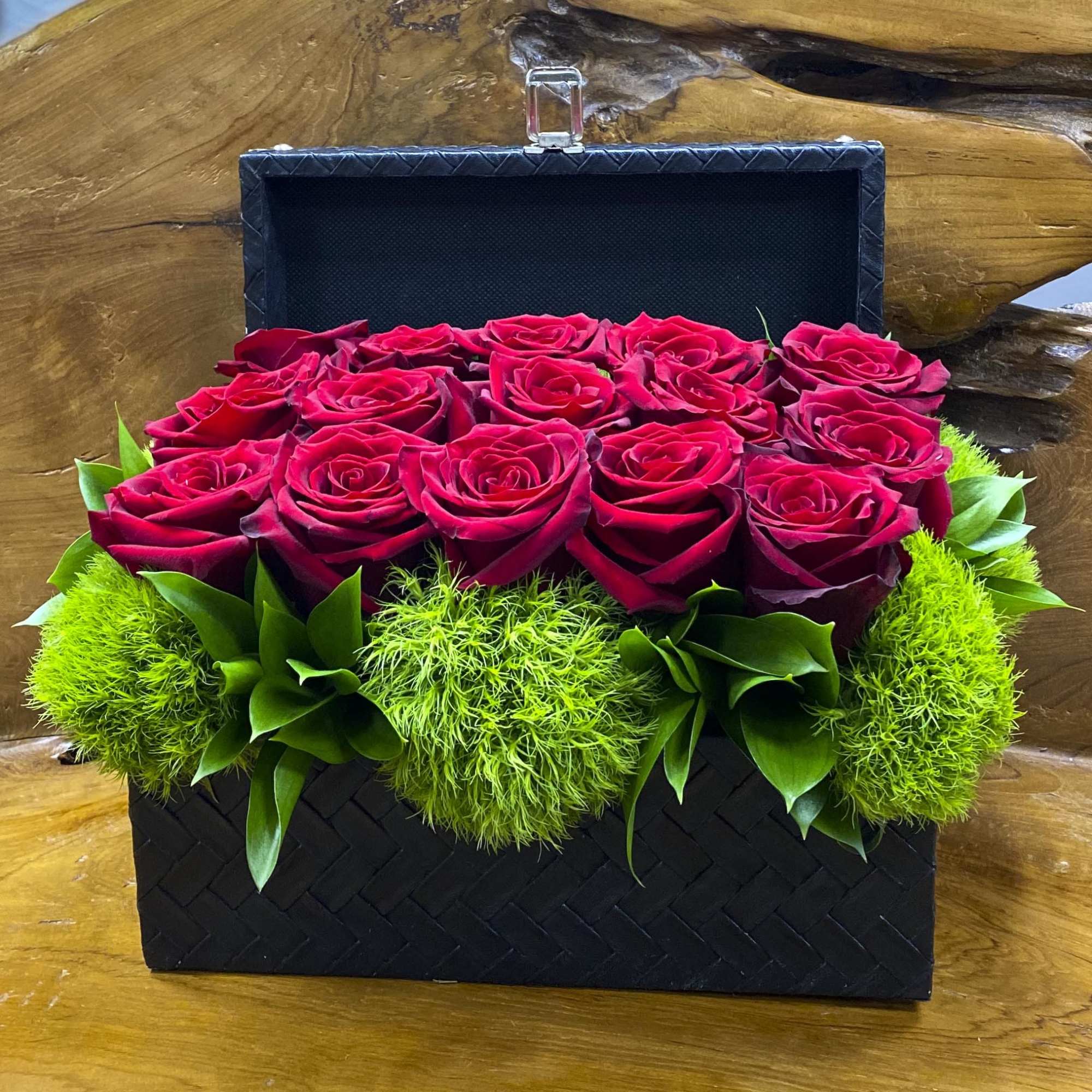 Red roses arranged in a black gift box with bright green accents