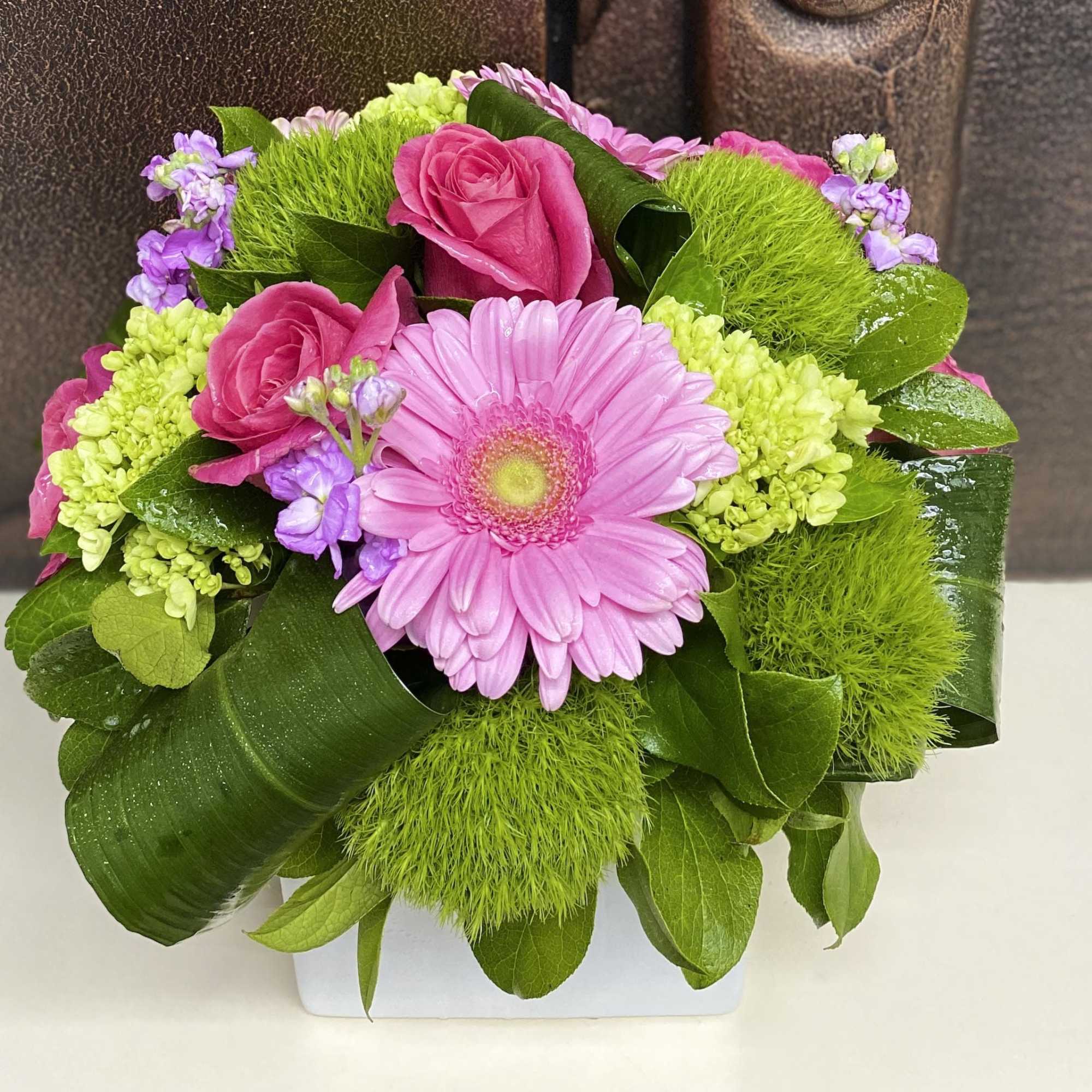 Pink roses and a gerbera daisy in a white container