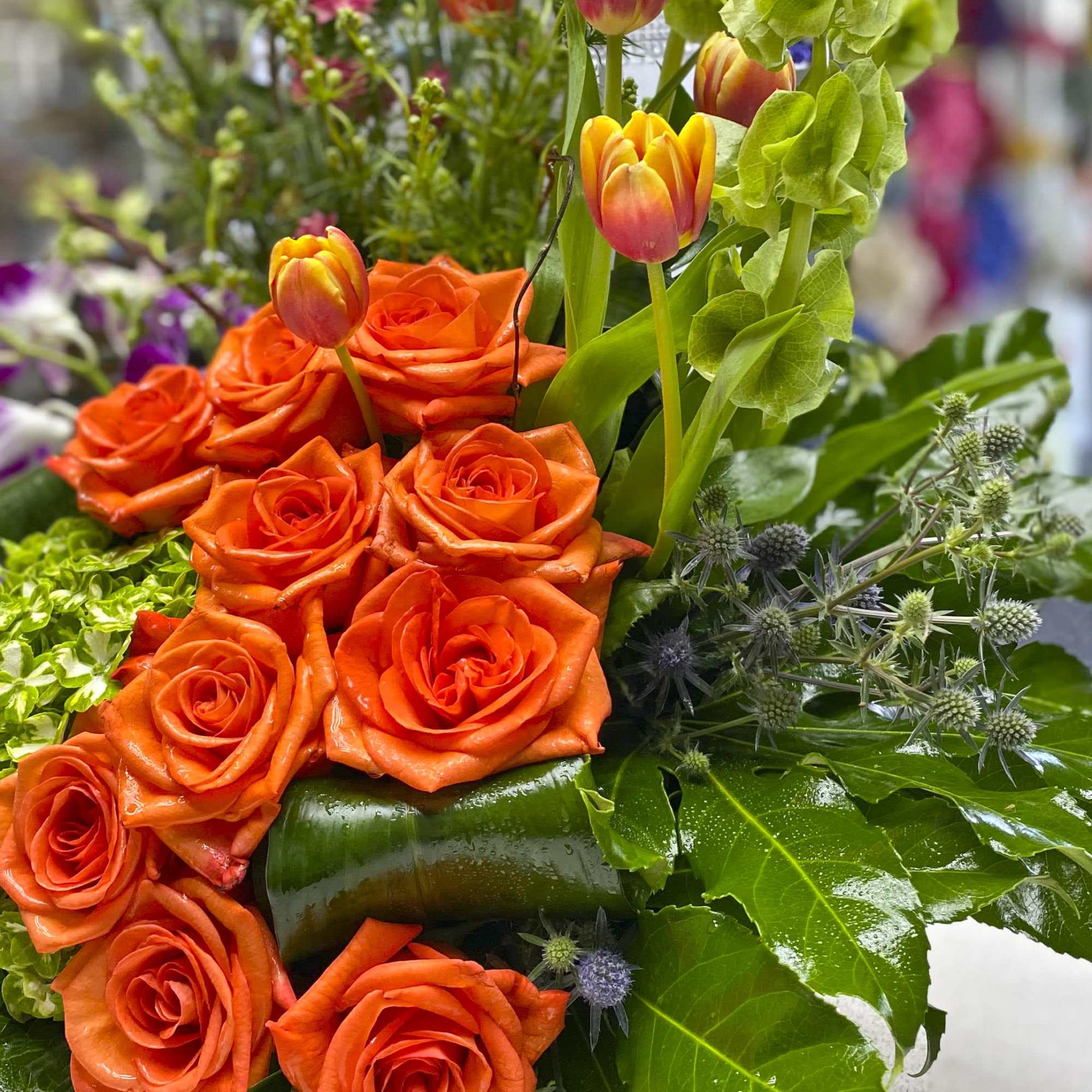 Orange roses with tulips and green foliage in a bouquet.