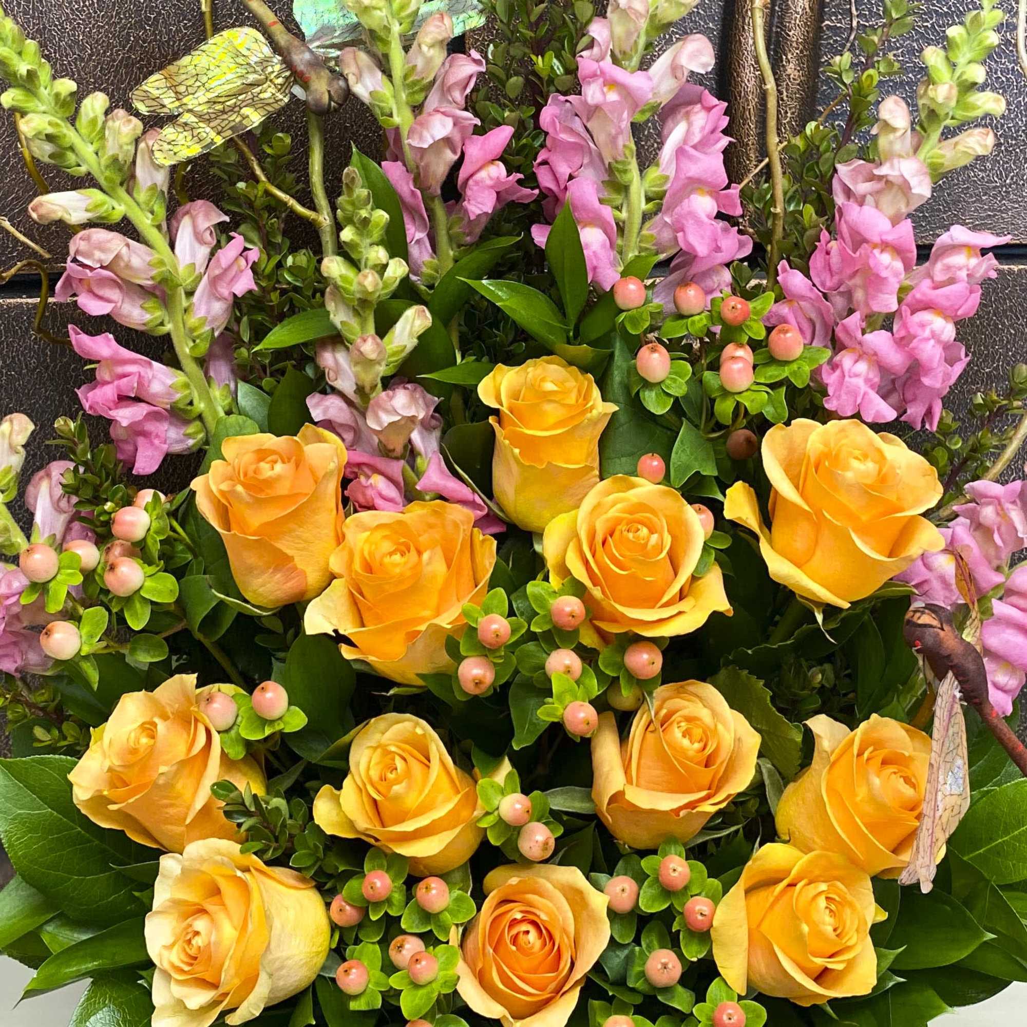 Yellow roses with pink snapdragons and berry accents in a floral arrangement.