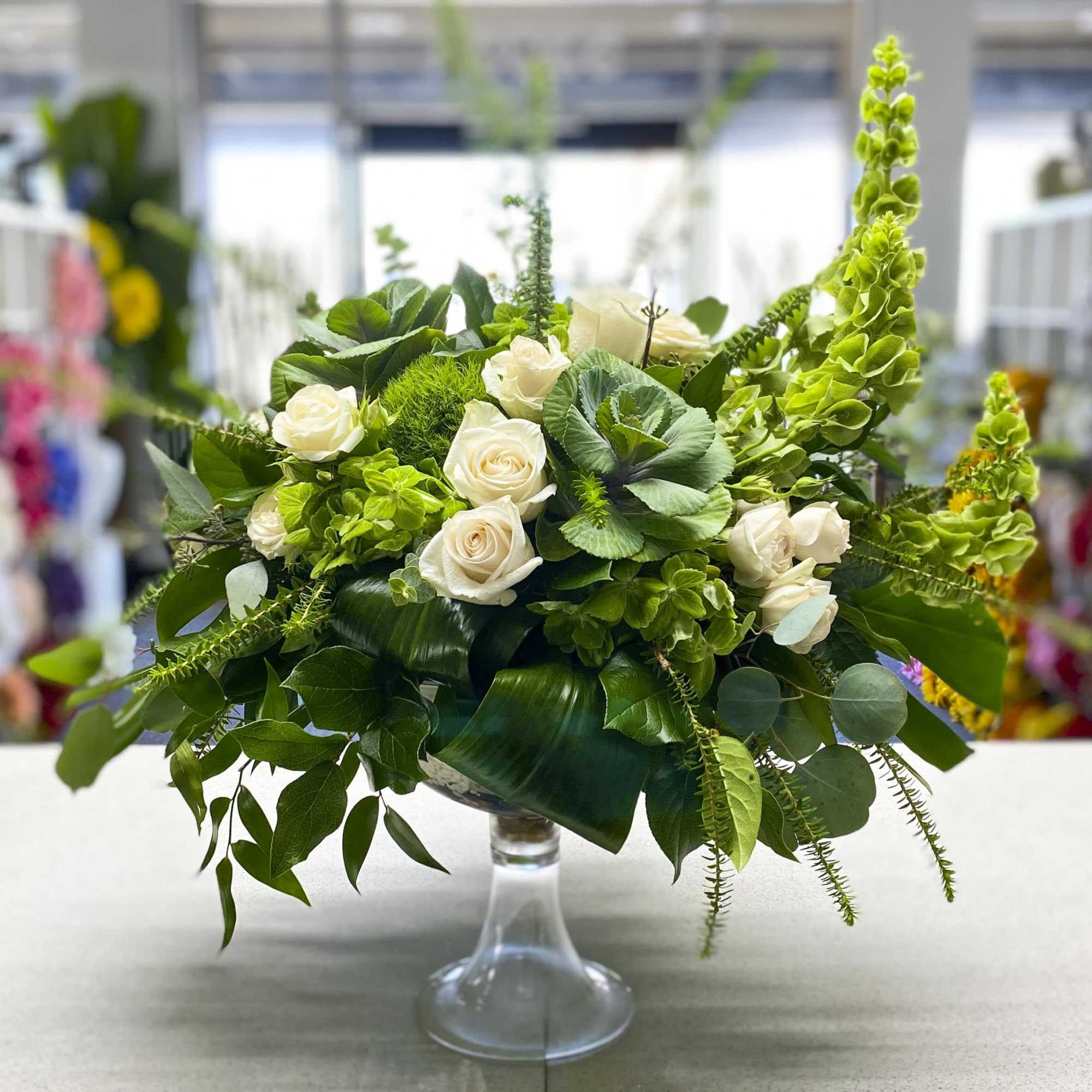 White roses and green flowers arranged in a clear glass vase