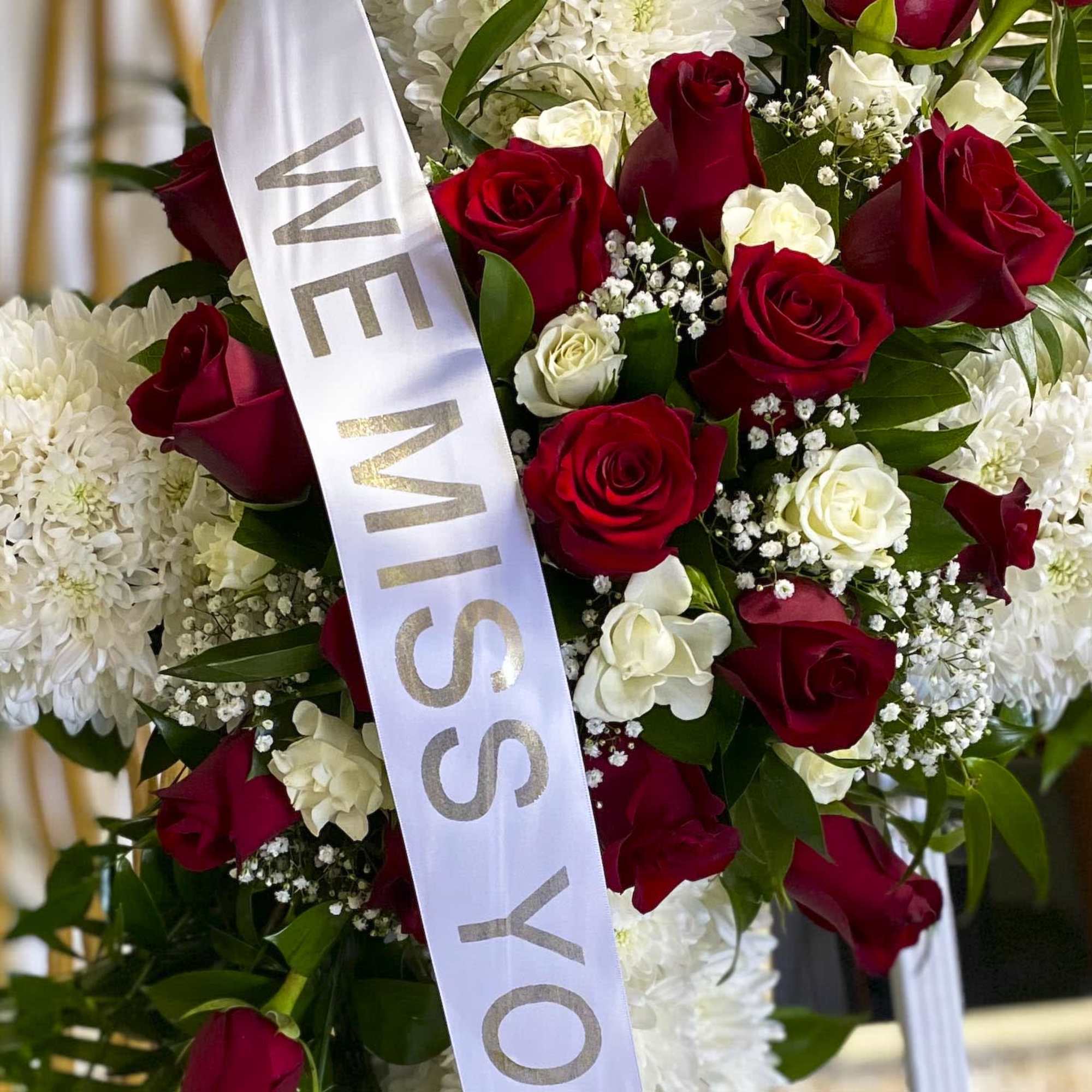Red and white rose arrangement with a white memorial ribbon