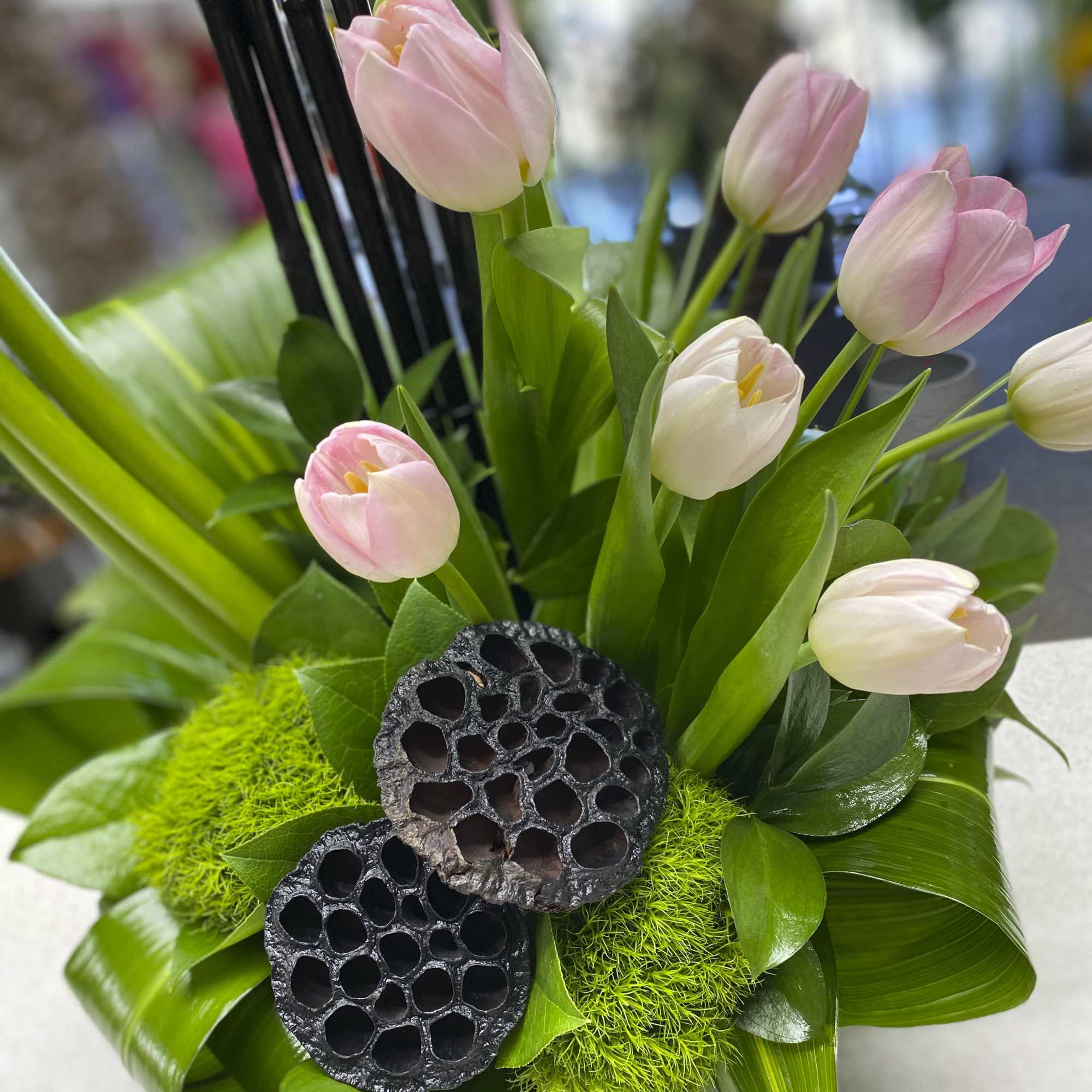 Pink and white tulips arranged with green foliage and dark seed pods