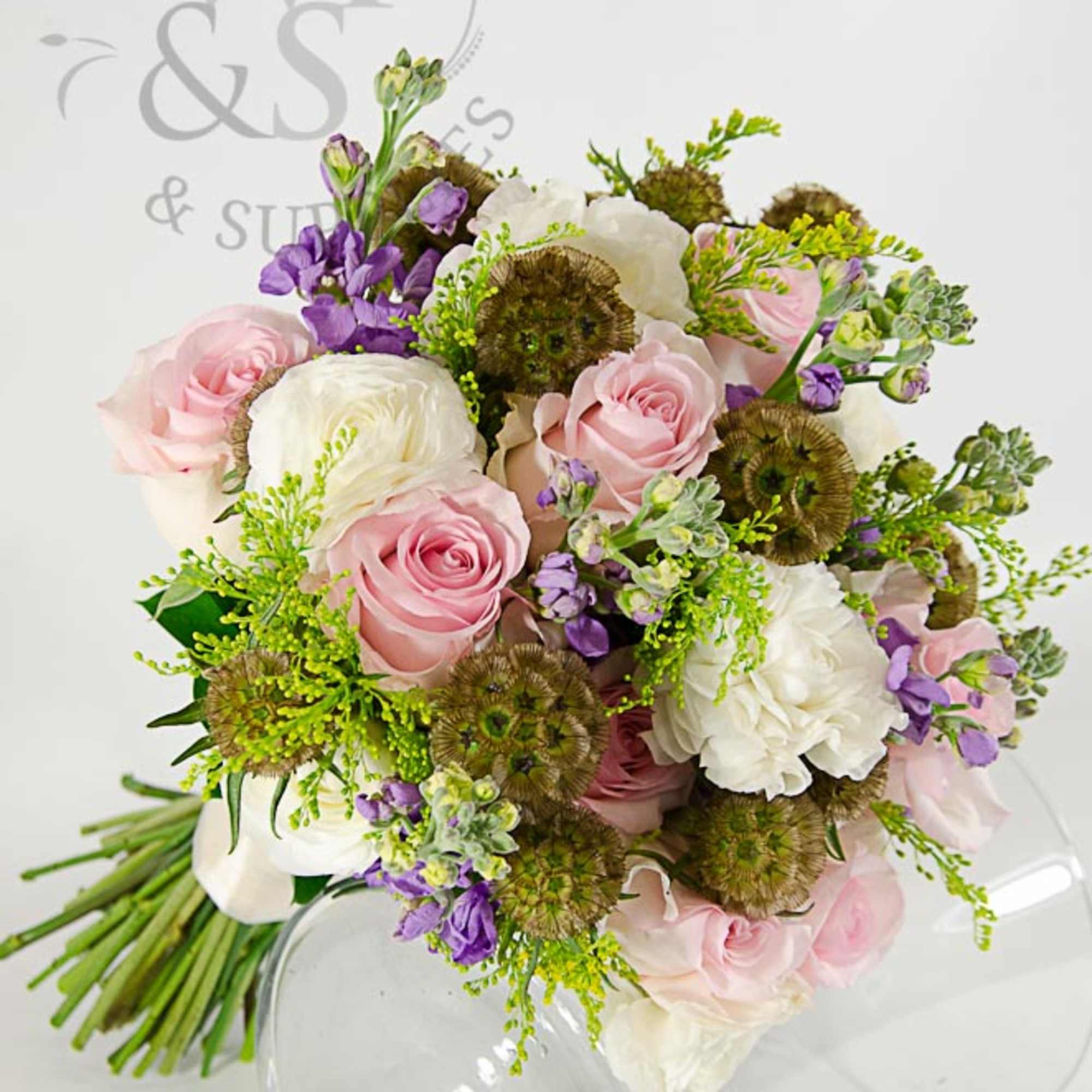 Bouquet of pink and white roses with purple accents in a clear glass vase