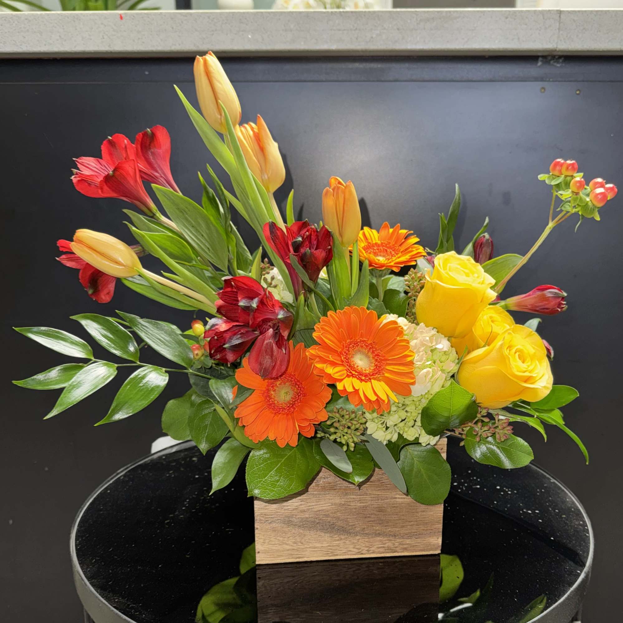 Mixed bouquet with yellow roses, gerbera daisies, and red-orange tulips in a wooden box