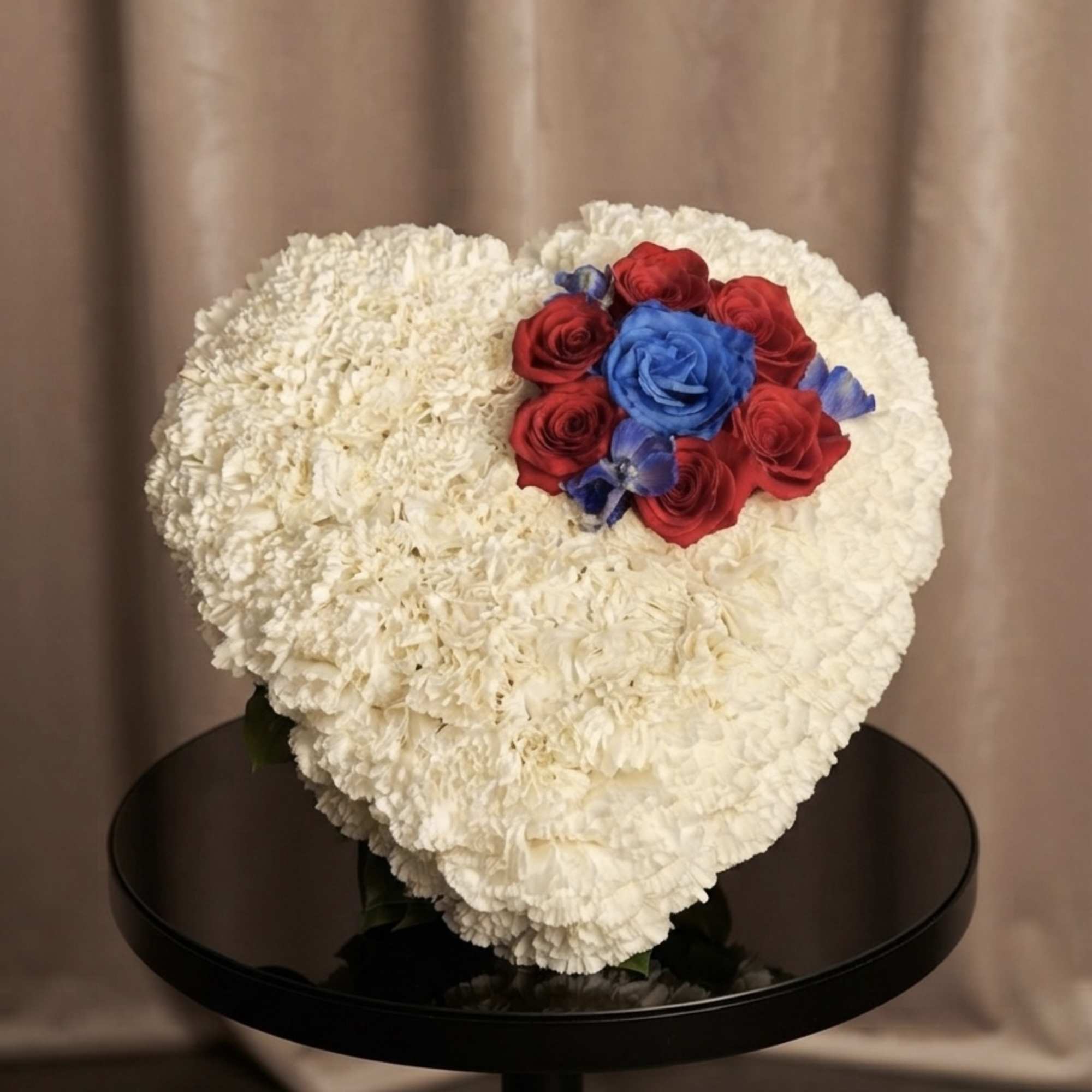 Heart-shaped white floral arrangement with red and blue roses
