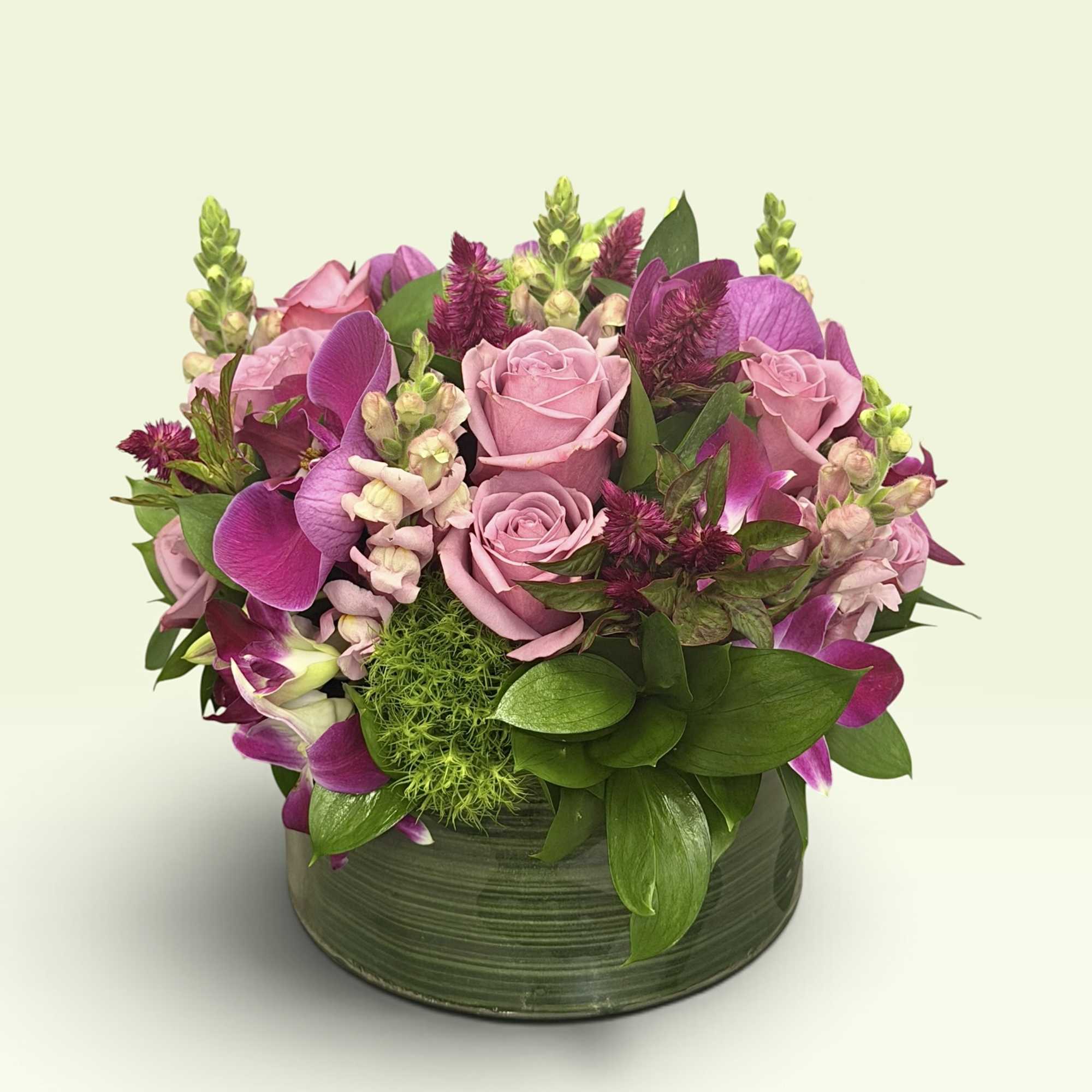 Pink roses and purple orchids arranged in a green round vase