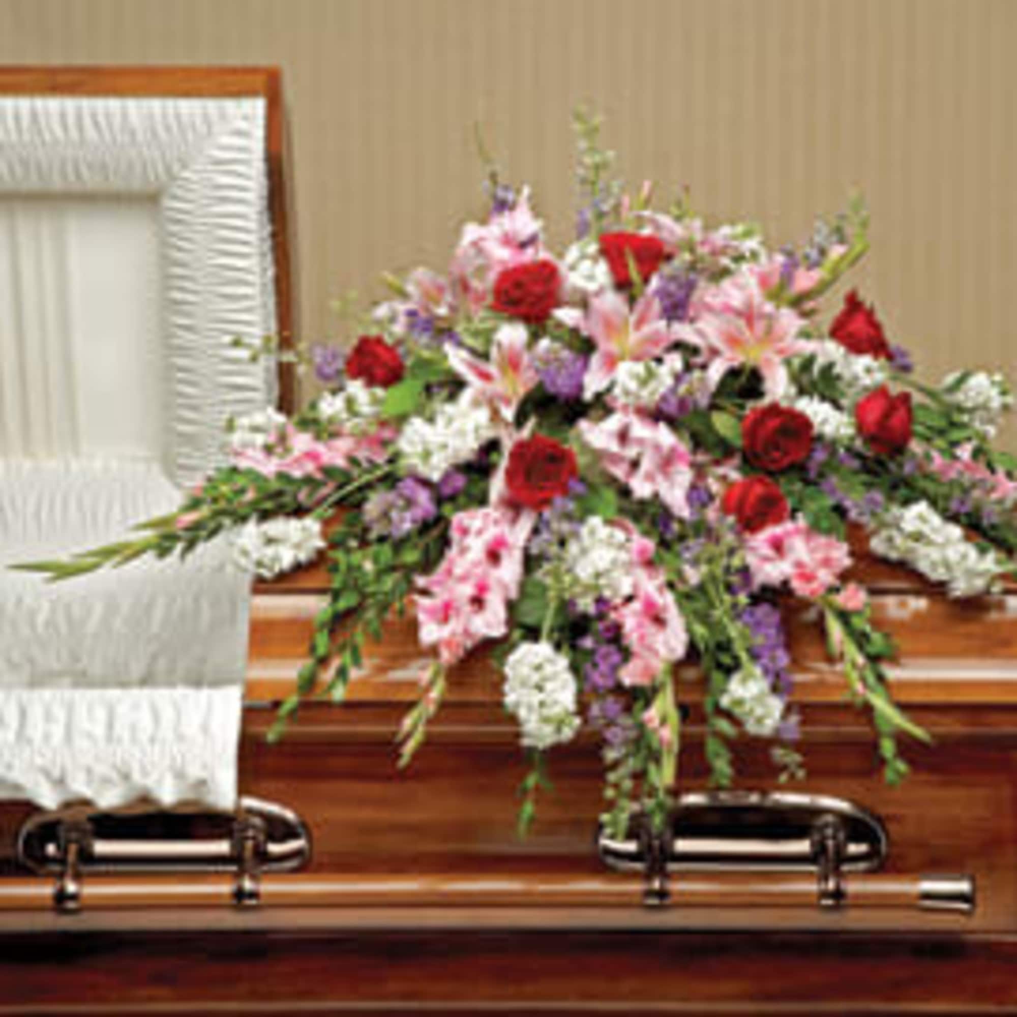 Floral casket spray with pink lilies, red roses, and white blooms