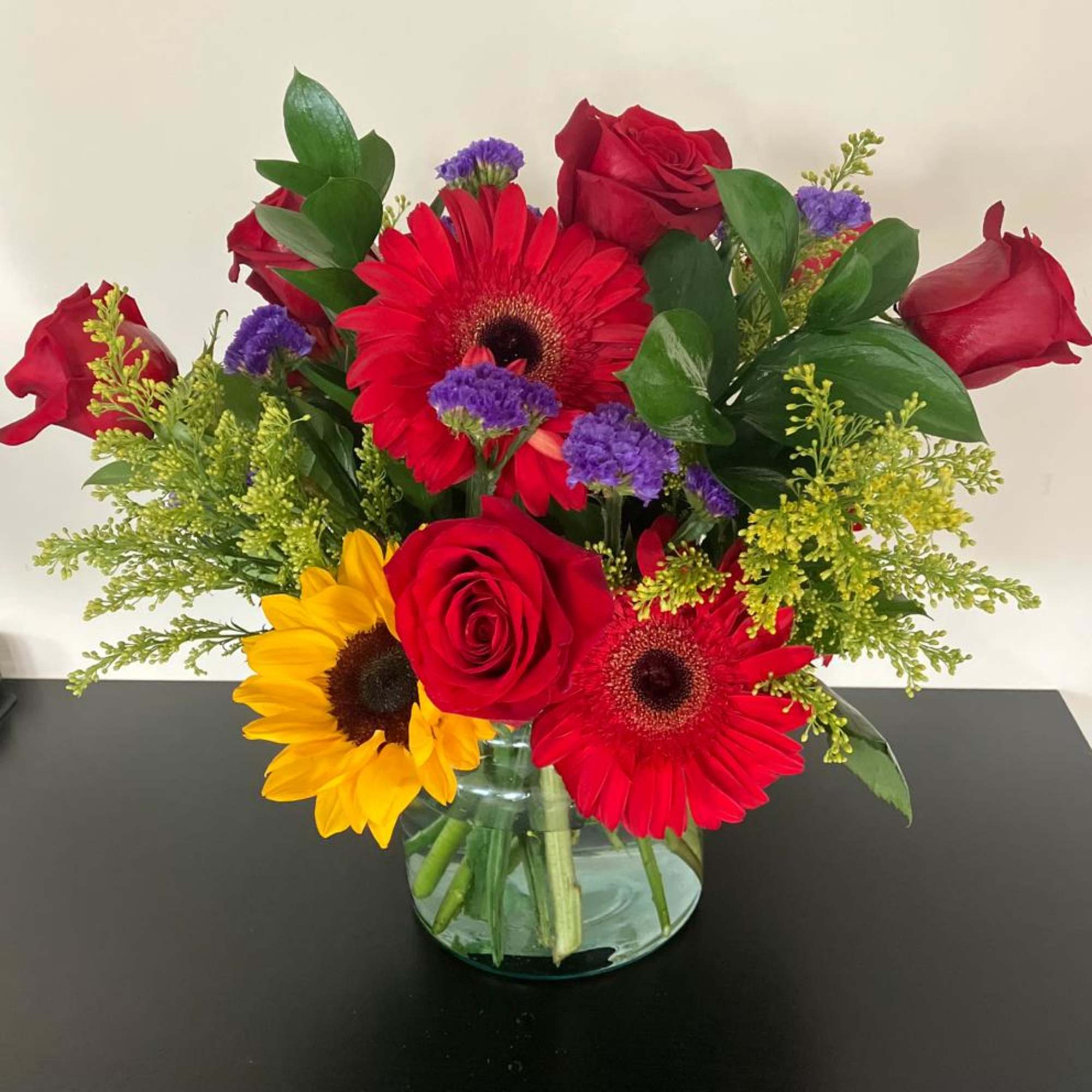 Bouquet of red roses, gerbera daisies, and a yellow sunflower in a glass vase