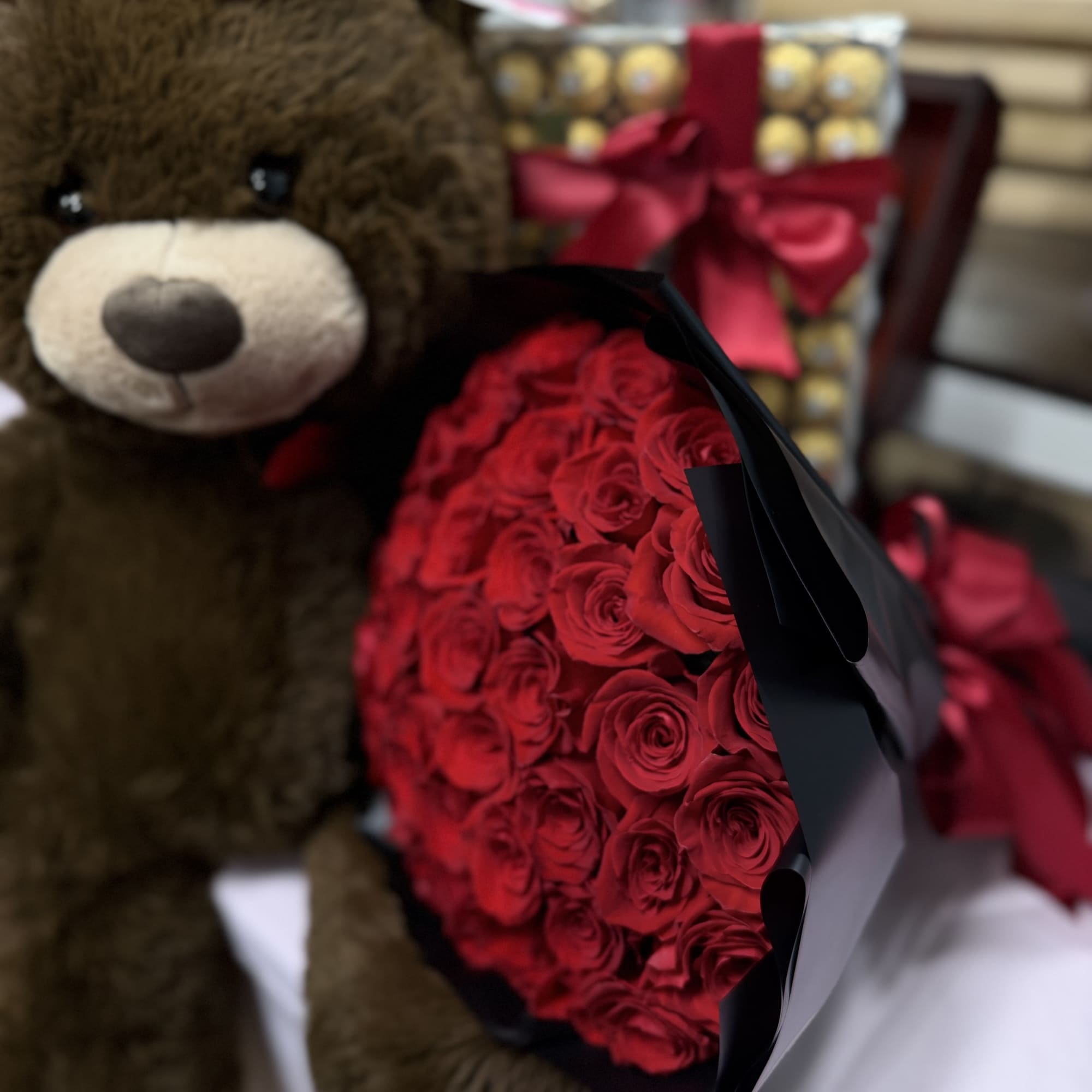 Teddy bear beside a bouquet of red roses and a gift box with a ribbon