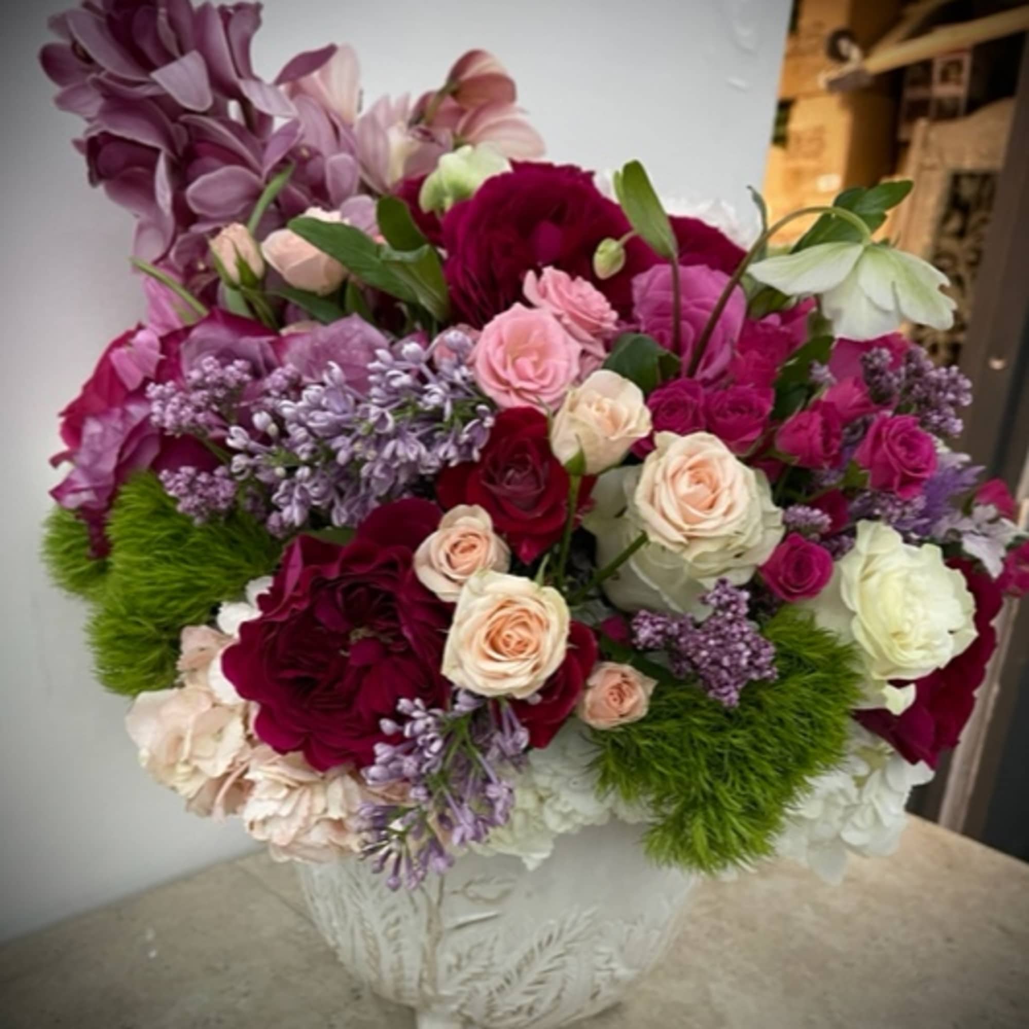 Bouquet of pink, purple, and white roses with lilac flowers in a white vase