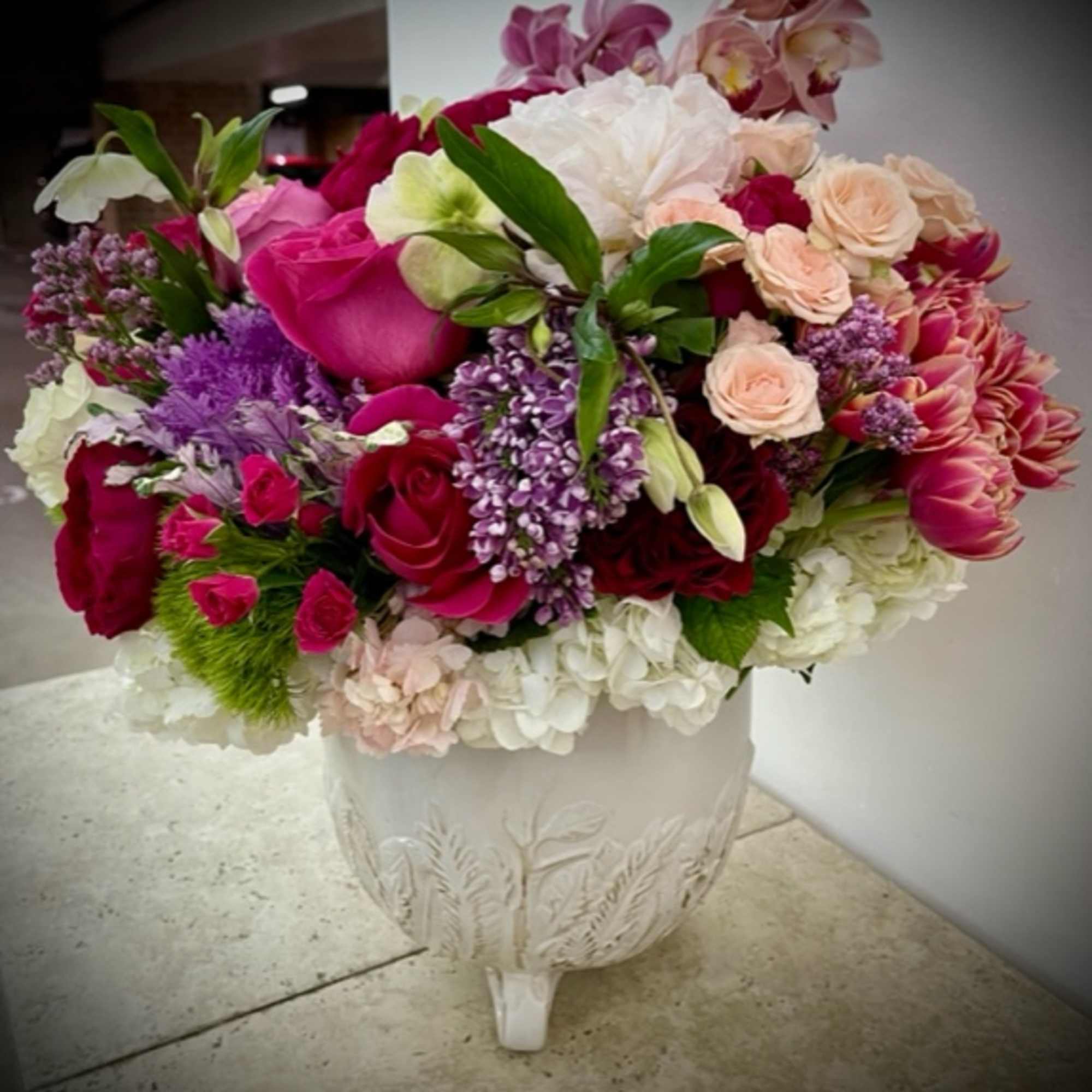 Mixed pink, white, and purple flowers arranged in a white pedestal vase.