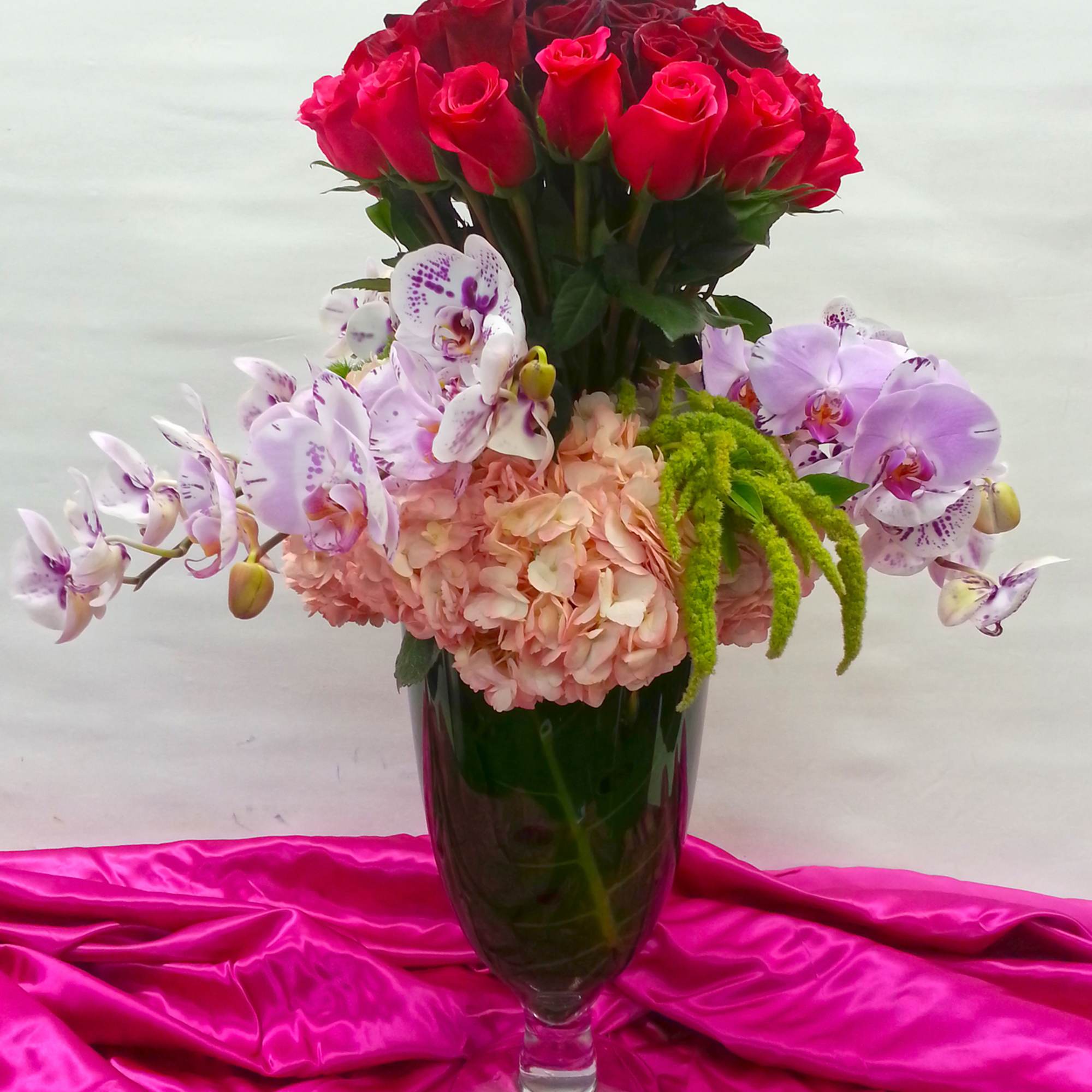 Bouquet of red roses, pink hydrangea, and orchids in a glass vase