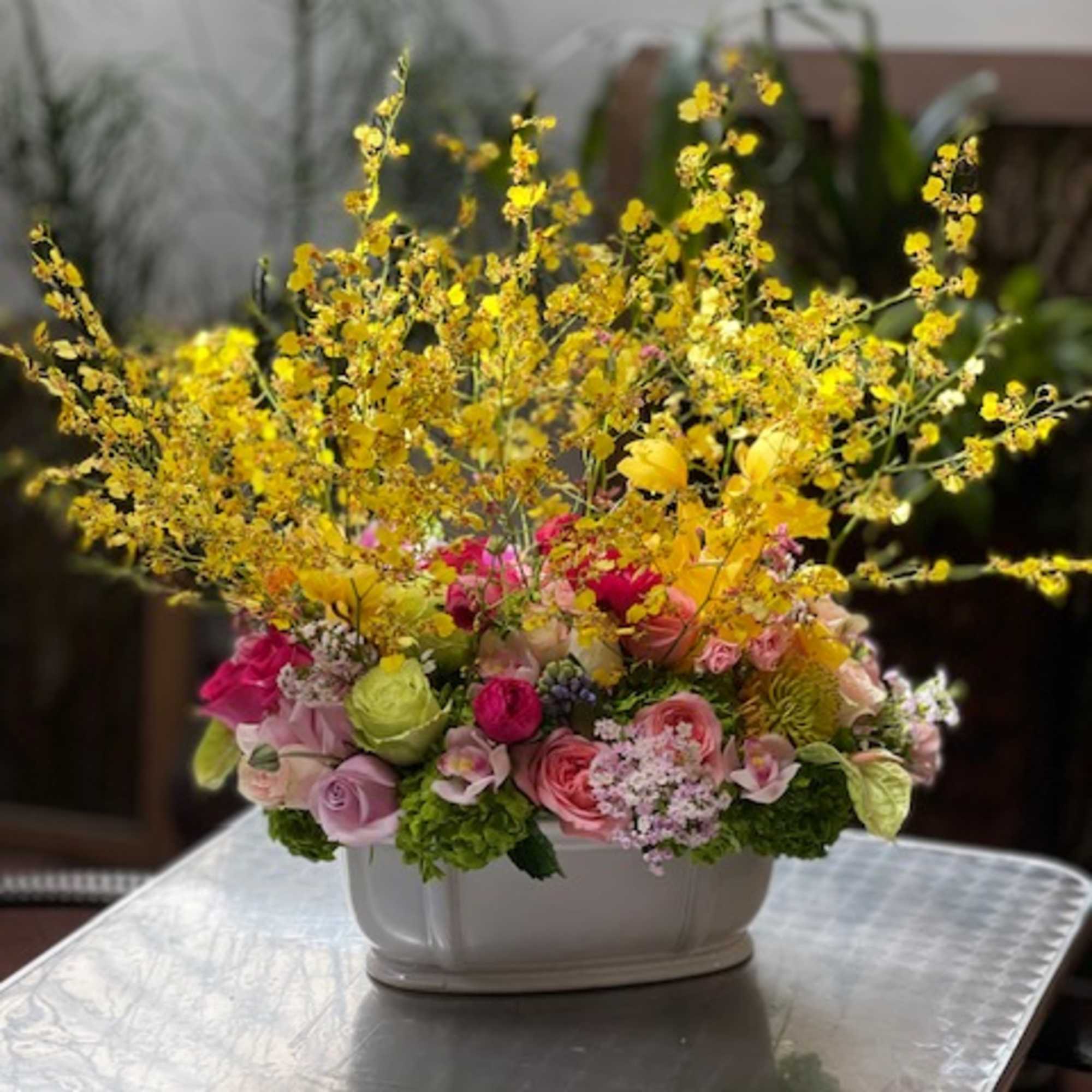 Colorful flower arrangement in a white container with tall yellow sprays