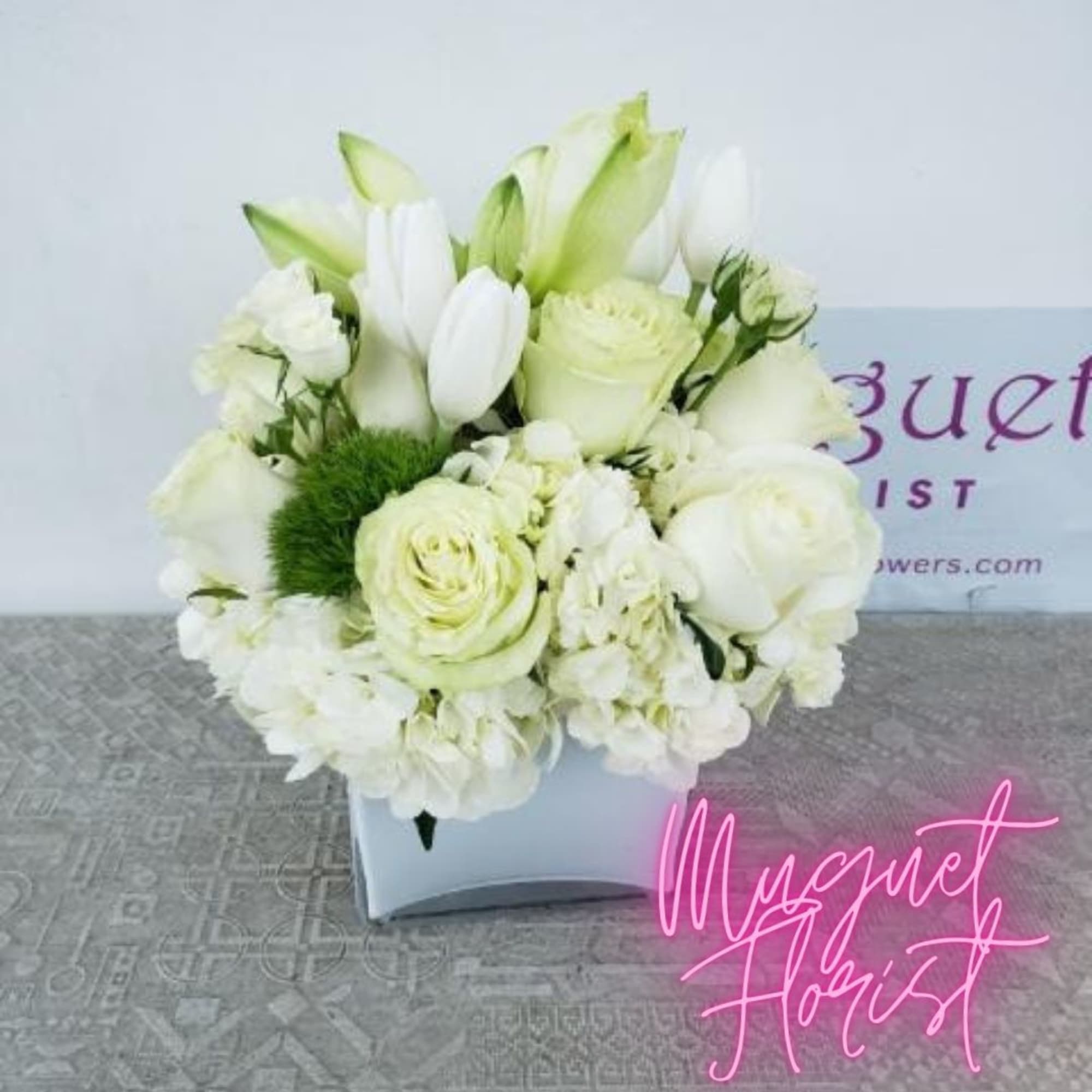 White floral arrangement in a square vase with green accents