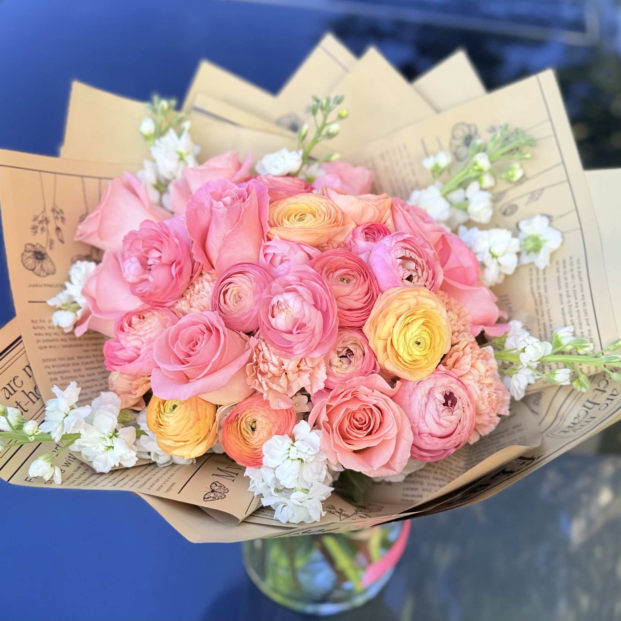 Bouquet of pink and yellow flowers wrapped in brown paper with a glass vase