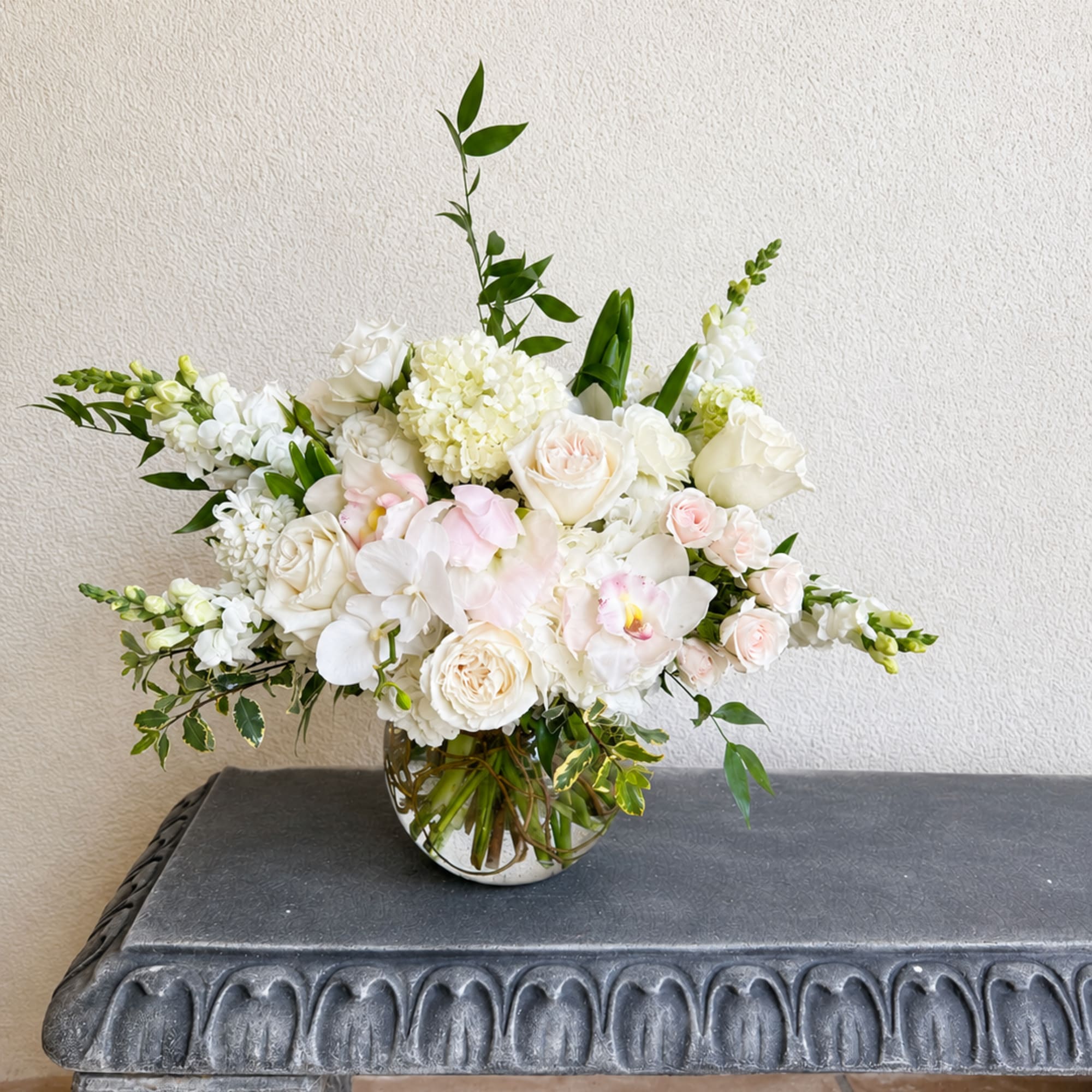White and blush floral arrangement in a round glass vase