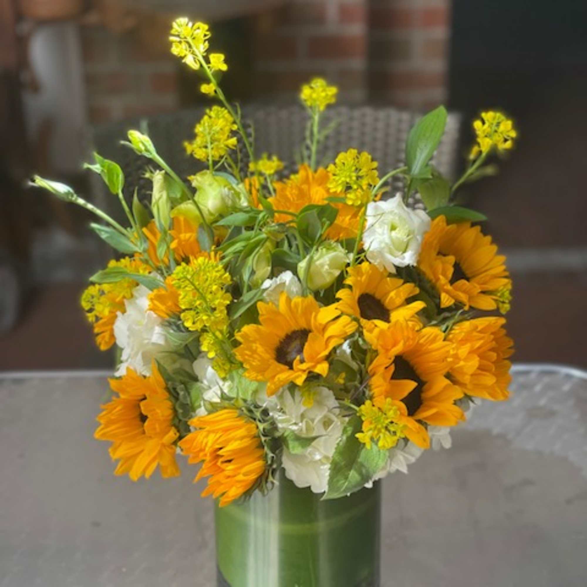 Sunflower and white flower arrangement in a green glass vase