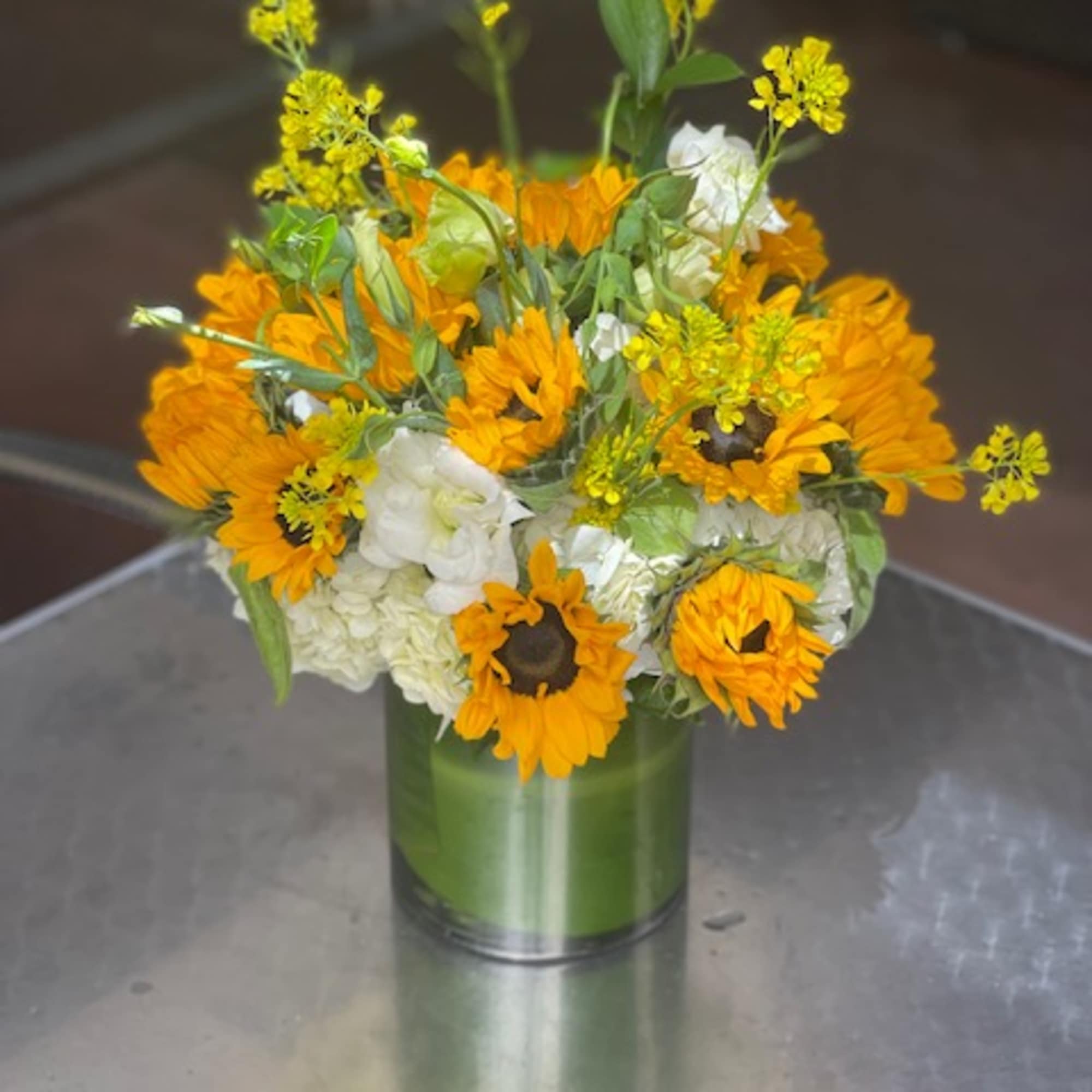 Orange sunflowers and white blooms arranged in a green glass vase.