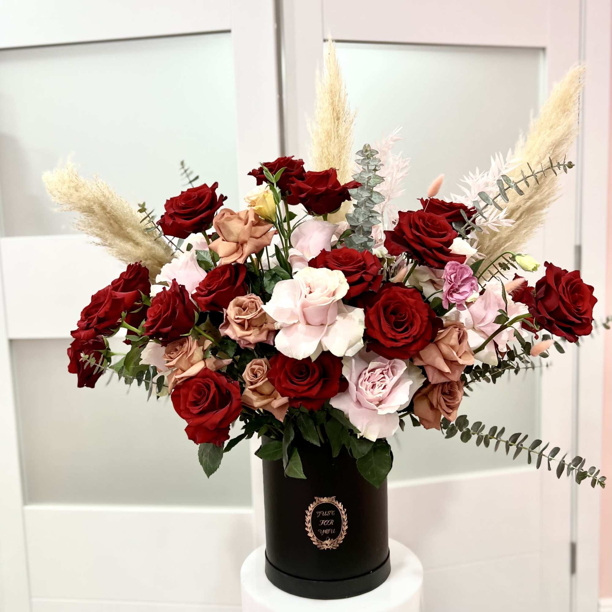 Red and blush roses arranged in a black hatbox with pampas grass