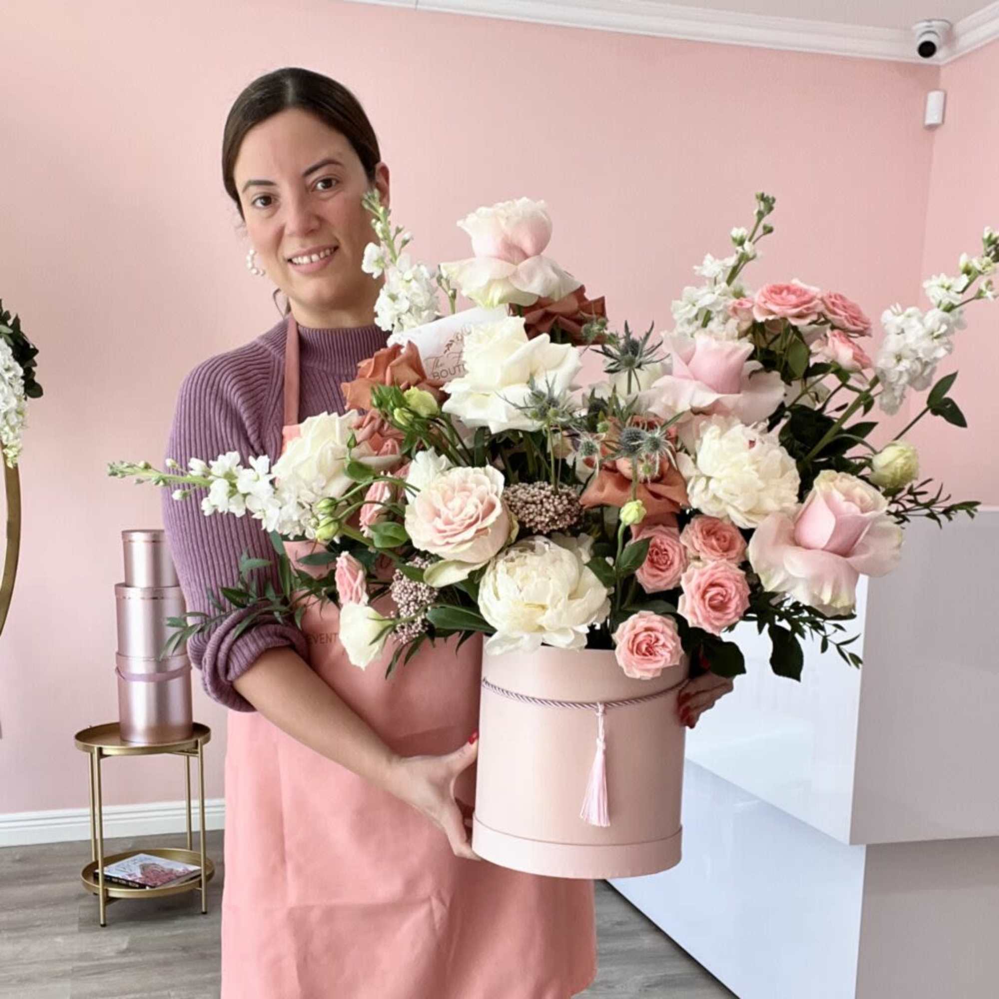 Woman holding a large pink hatbox arrangement of roses and white blooms
