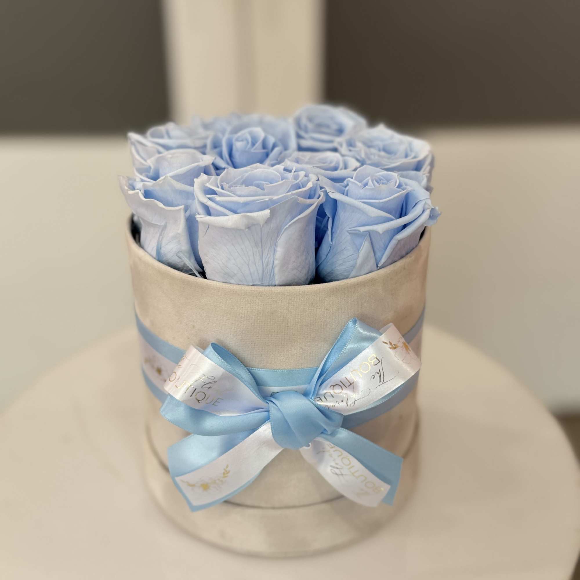 Blue roses arranged in a round hat box with a satin ribbon bow