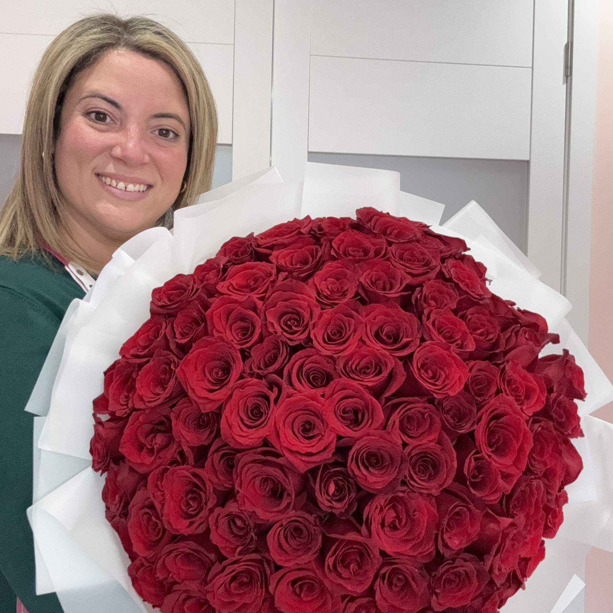 Woman holding a large bouquet of red roses wrapped in white paper