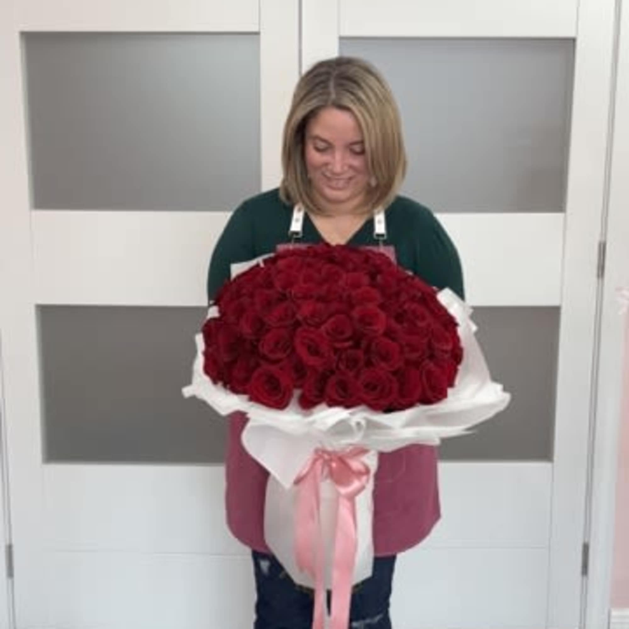 Woman holding a large bouquet of red roses wrapped in white paper with a pink ribbon