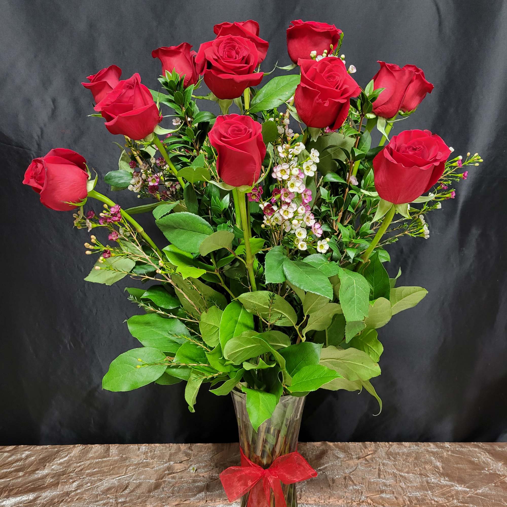 Red roses arranged in a clear glass vase with a red ribbon