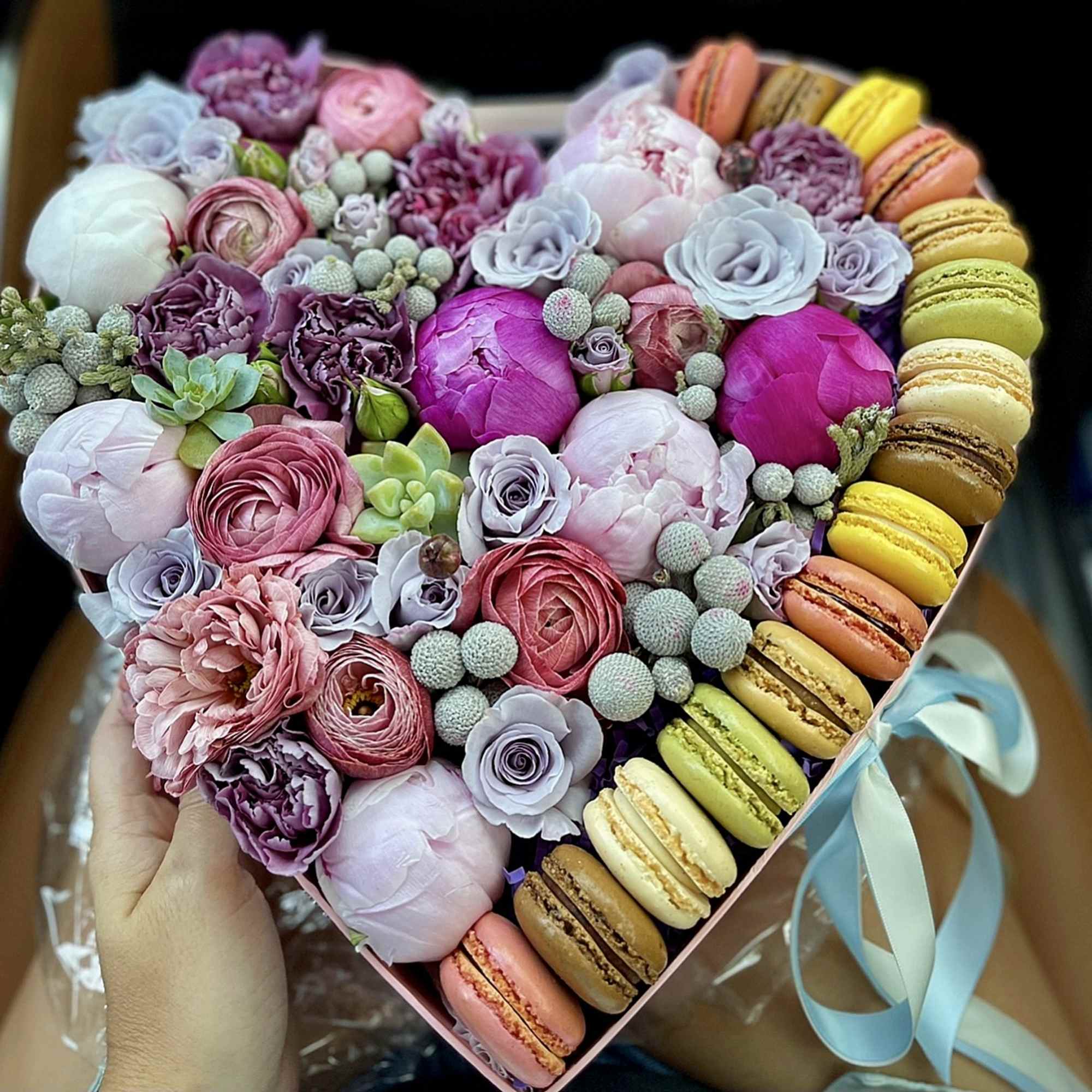 Heart-shaped box of pastel flowers with macarons around the edge