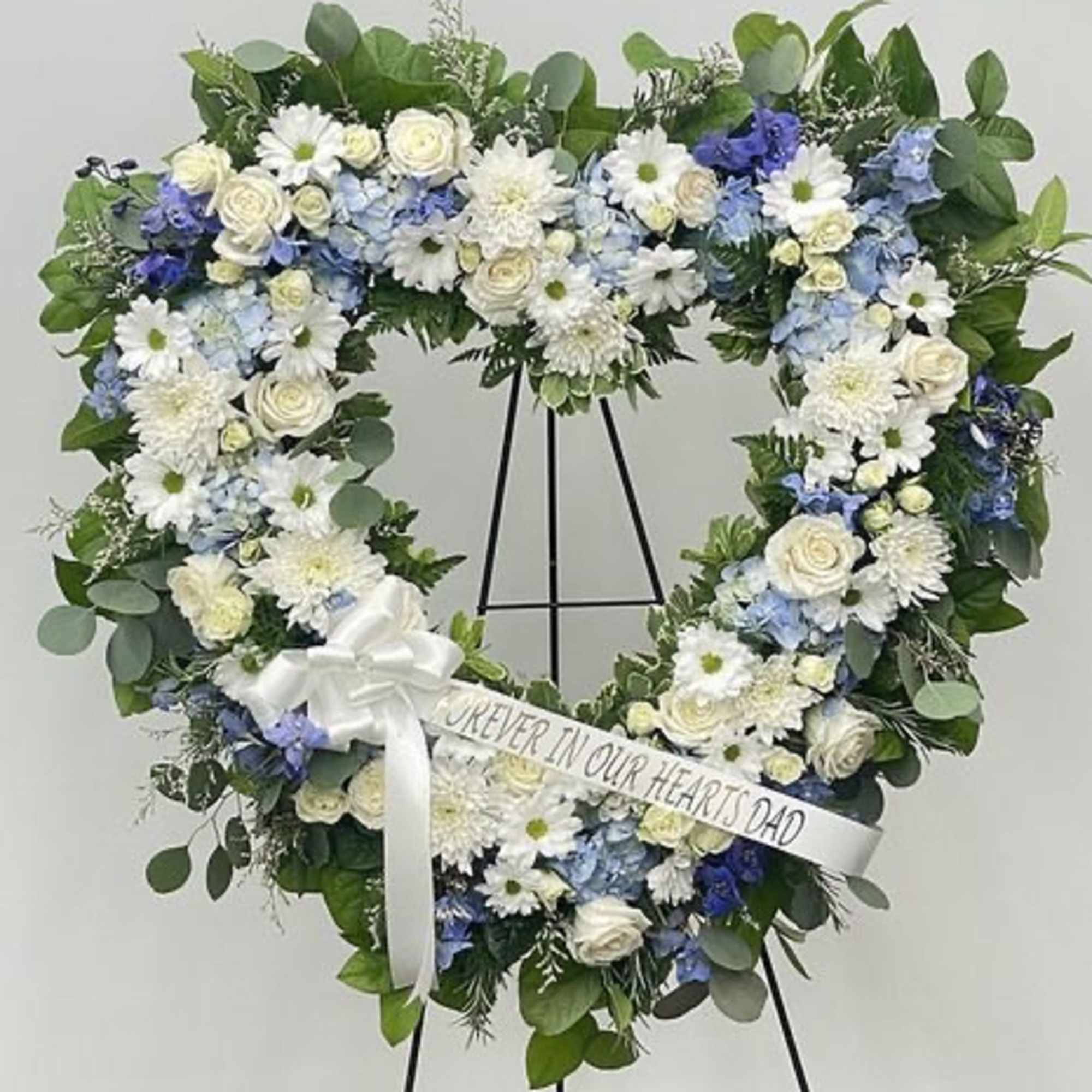 Heart-shaped floral wreath on a stand with a white ribbon